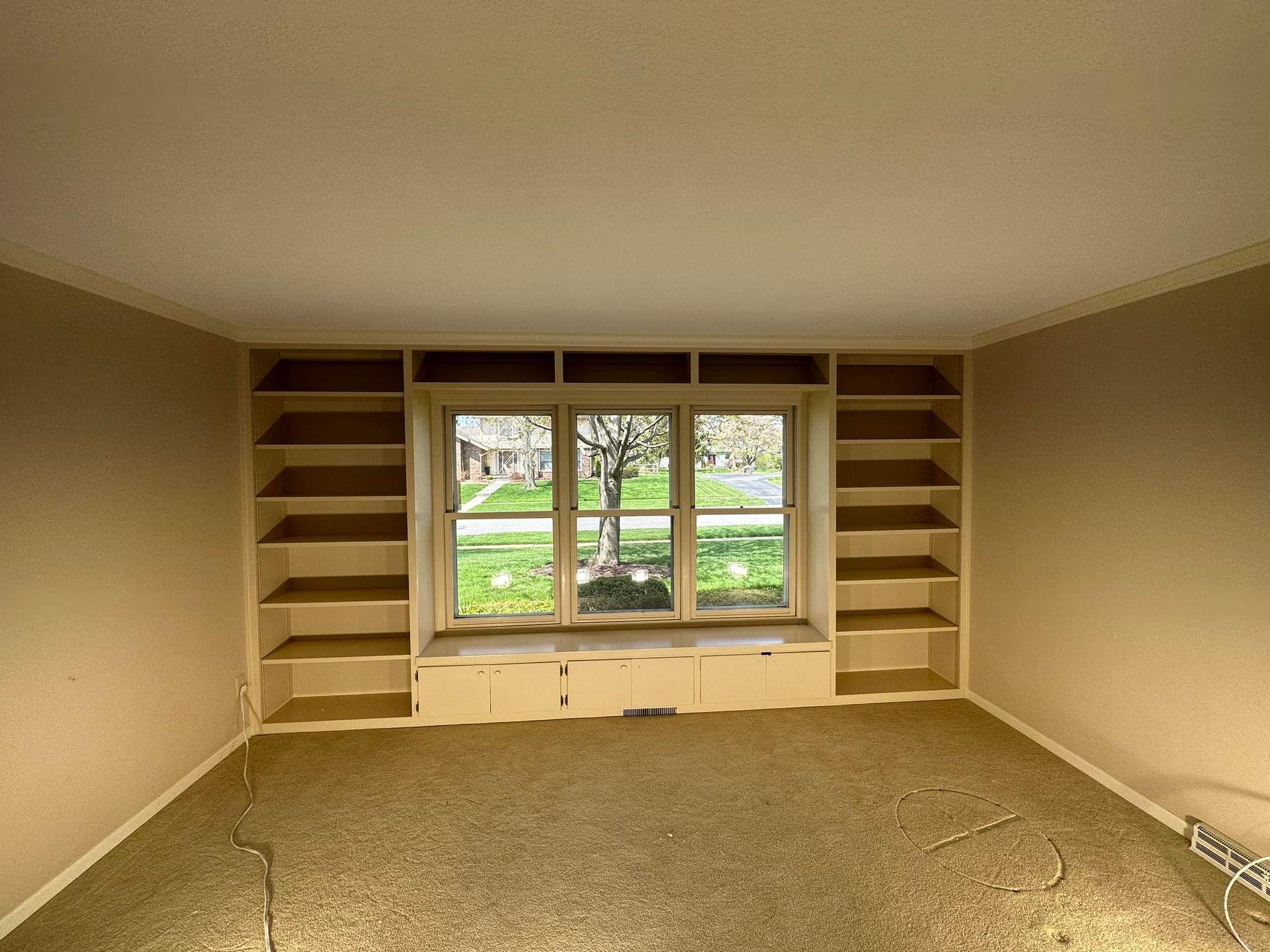 Empty room with built-in bookshelves flanking a window with a view of a tree and lawn.