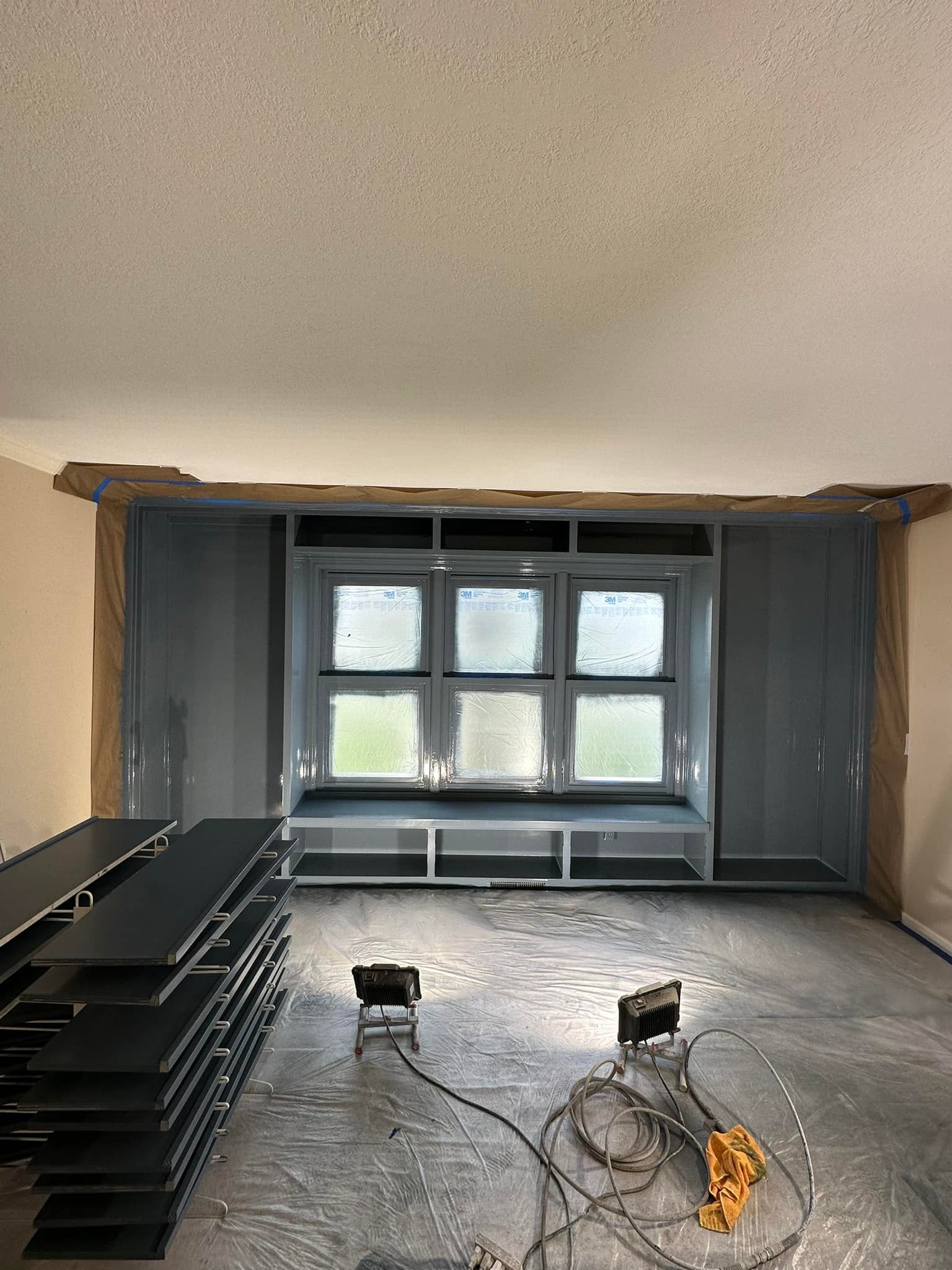 Interior room with a bay window under construction; gray walls and window frame, stacks of flooring, and tools.