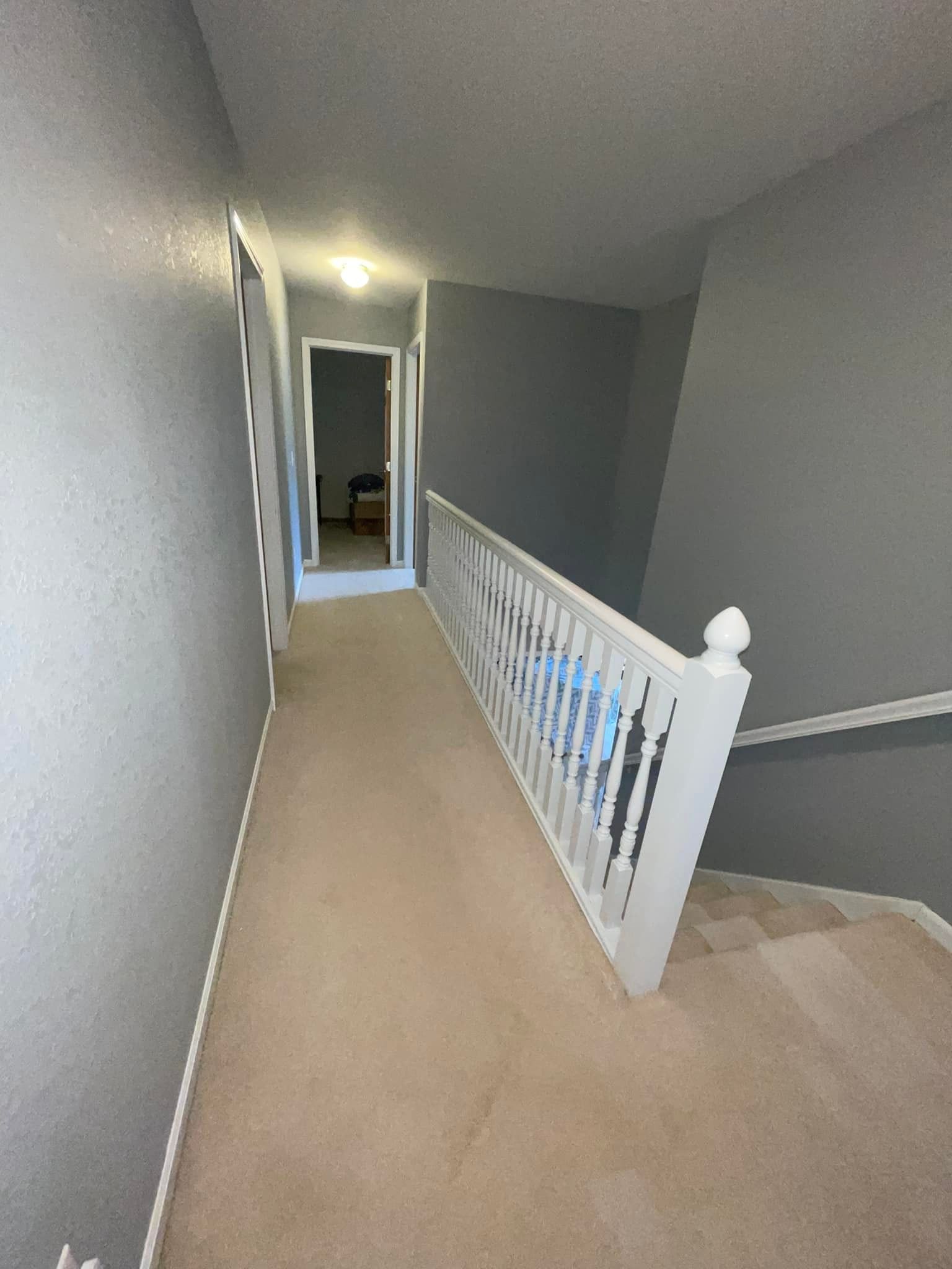 Hallway with carpet, gray walls, and white railing leading to a doorway.