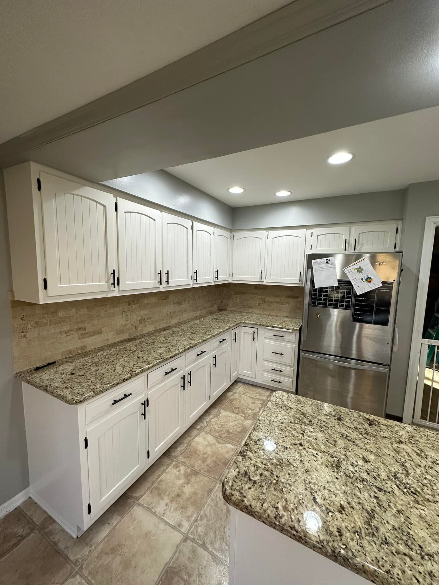 White kitchen cabinets with black hardware and granite countertops.