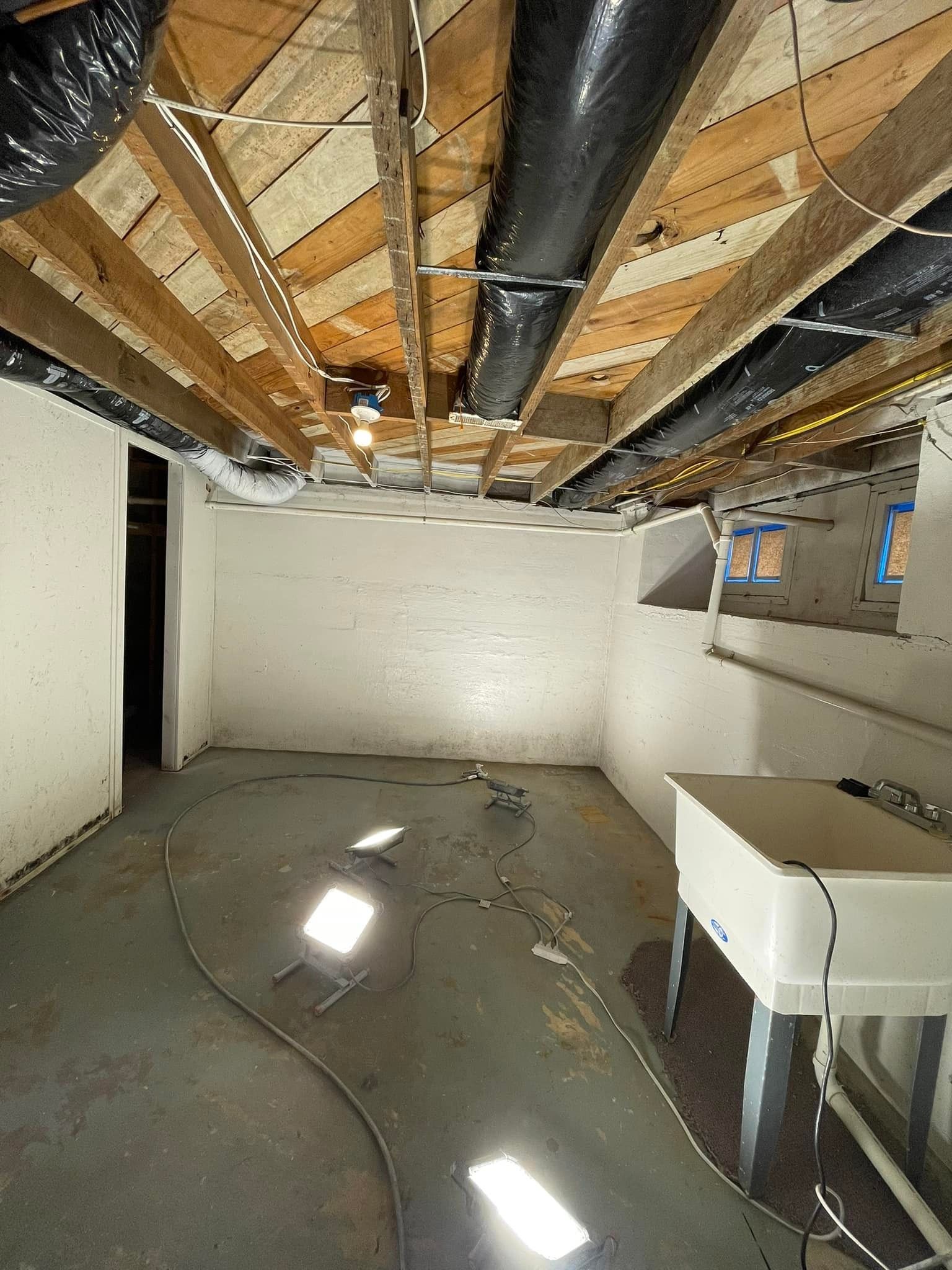 Basement room with concrete floor, exposed ceiling beams, ductwork, white walls, and a utility sink.