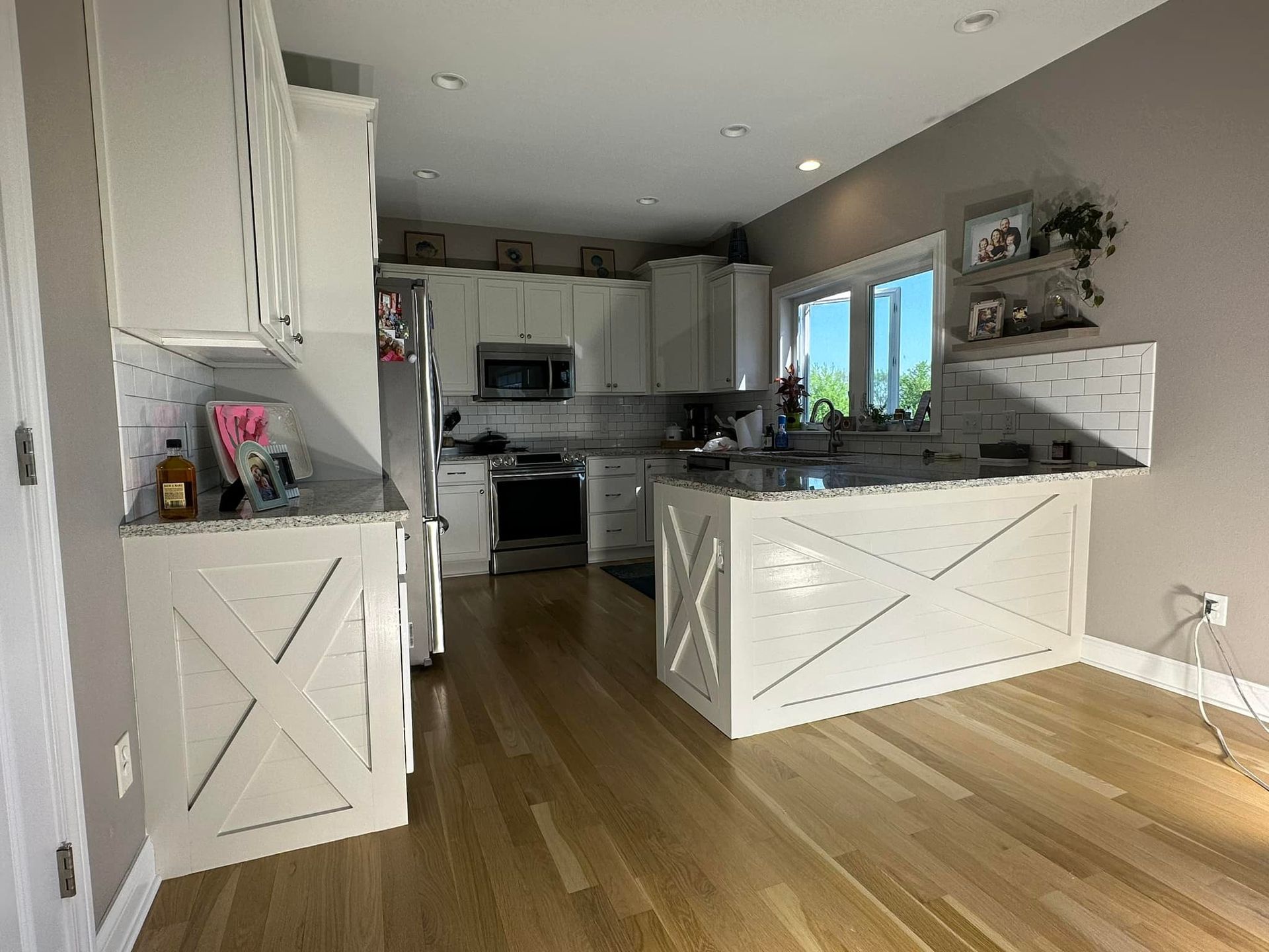 White kitchen with light wood floors, cabinets with X-shaped accents, granite countertops, and stainless steel appliances.