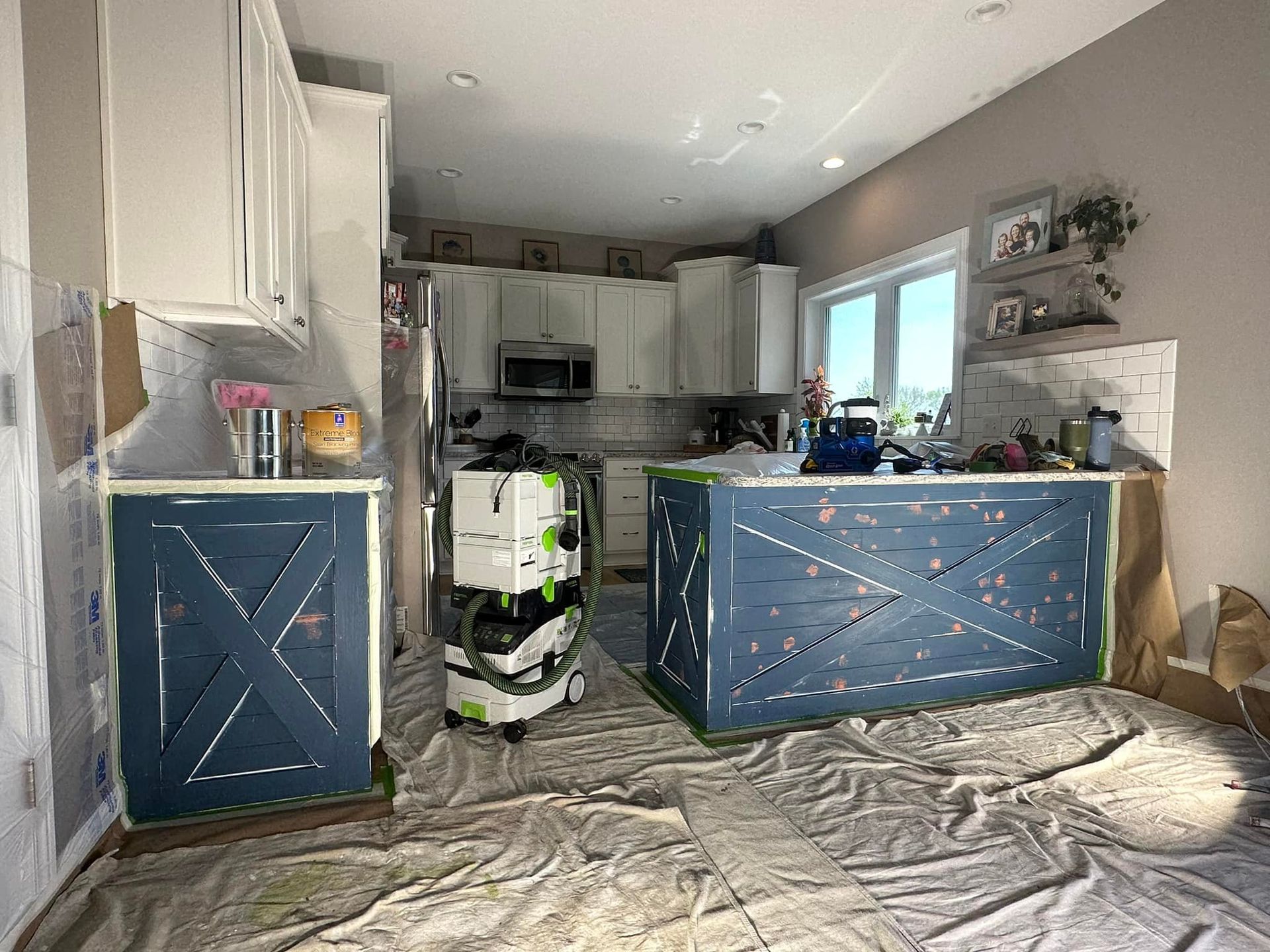 Kitchen undergoing renovation. Blue island and cabinet fronts being painted, cabinets white, with tools and drop cloths.