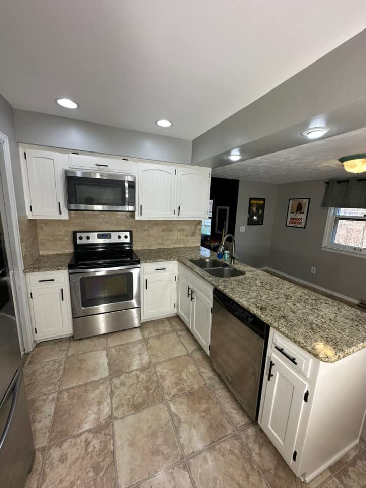White-cabinet kitchen with stainless appliances. Granite countertops, beige tile floor.