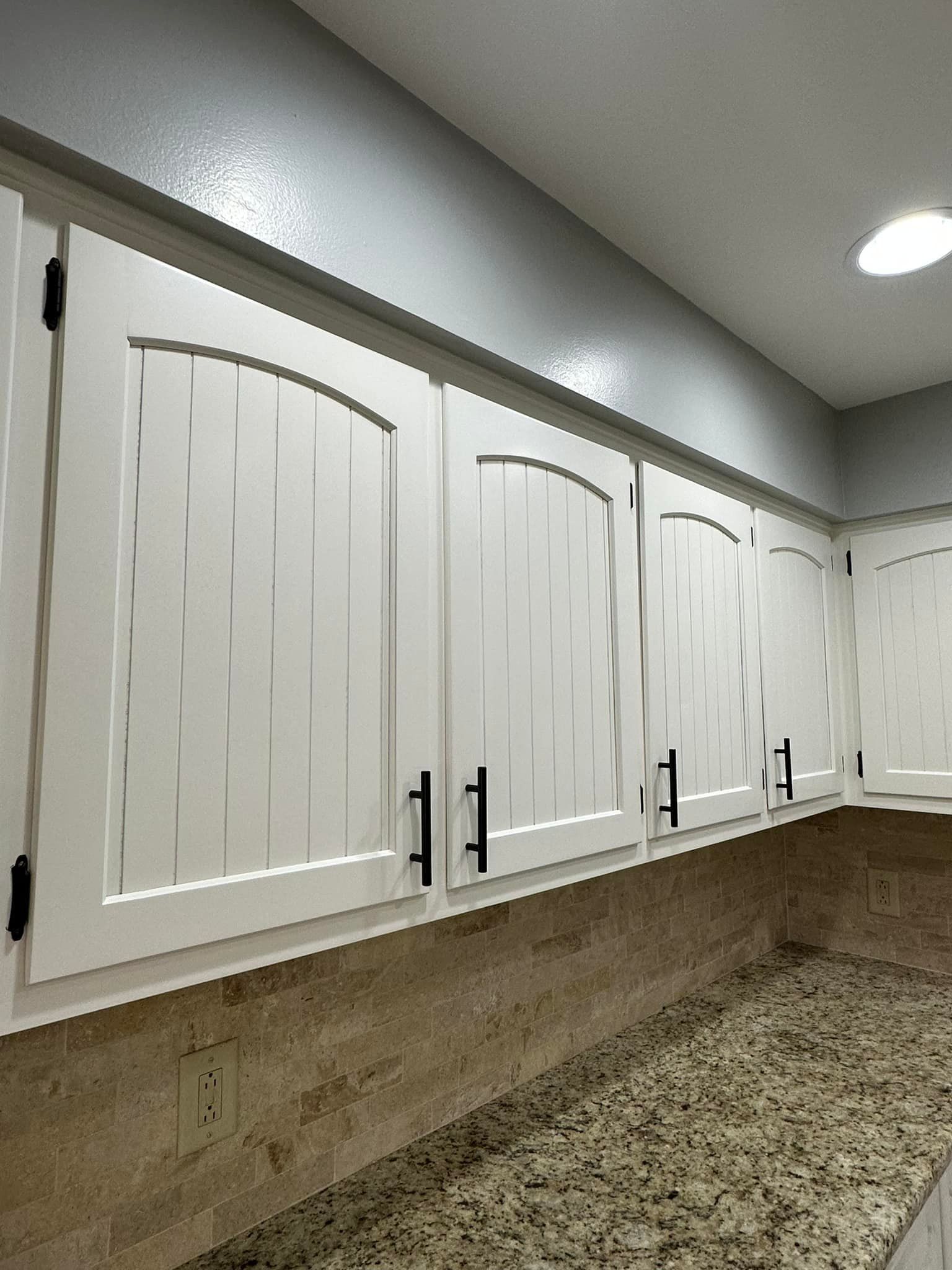 White kitchen cabinets with black handles, set against a granite countertop.