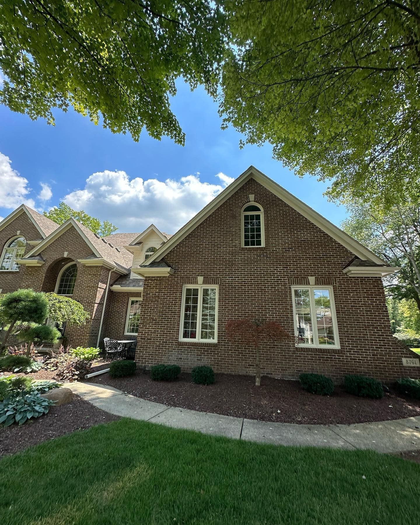 Brick house with arched and rectangular windows under a blue sky, surrounded by trees.
