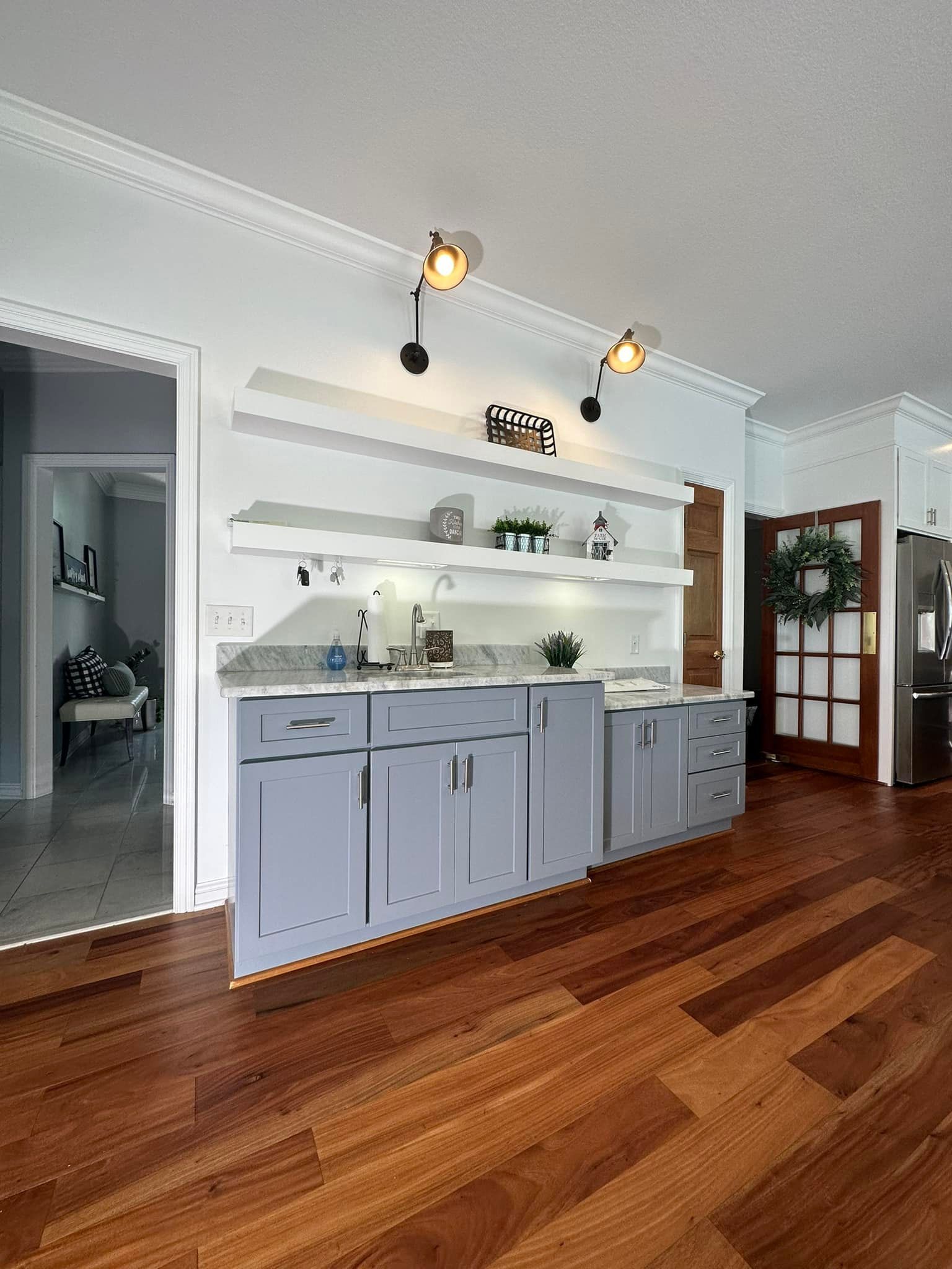 Gray cabinets with white countertops, open shelves, and track lighting in a kitchen area with hardwood floors.