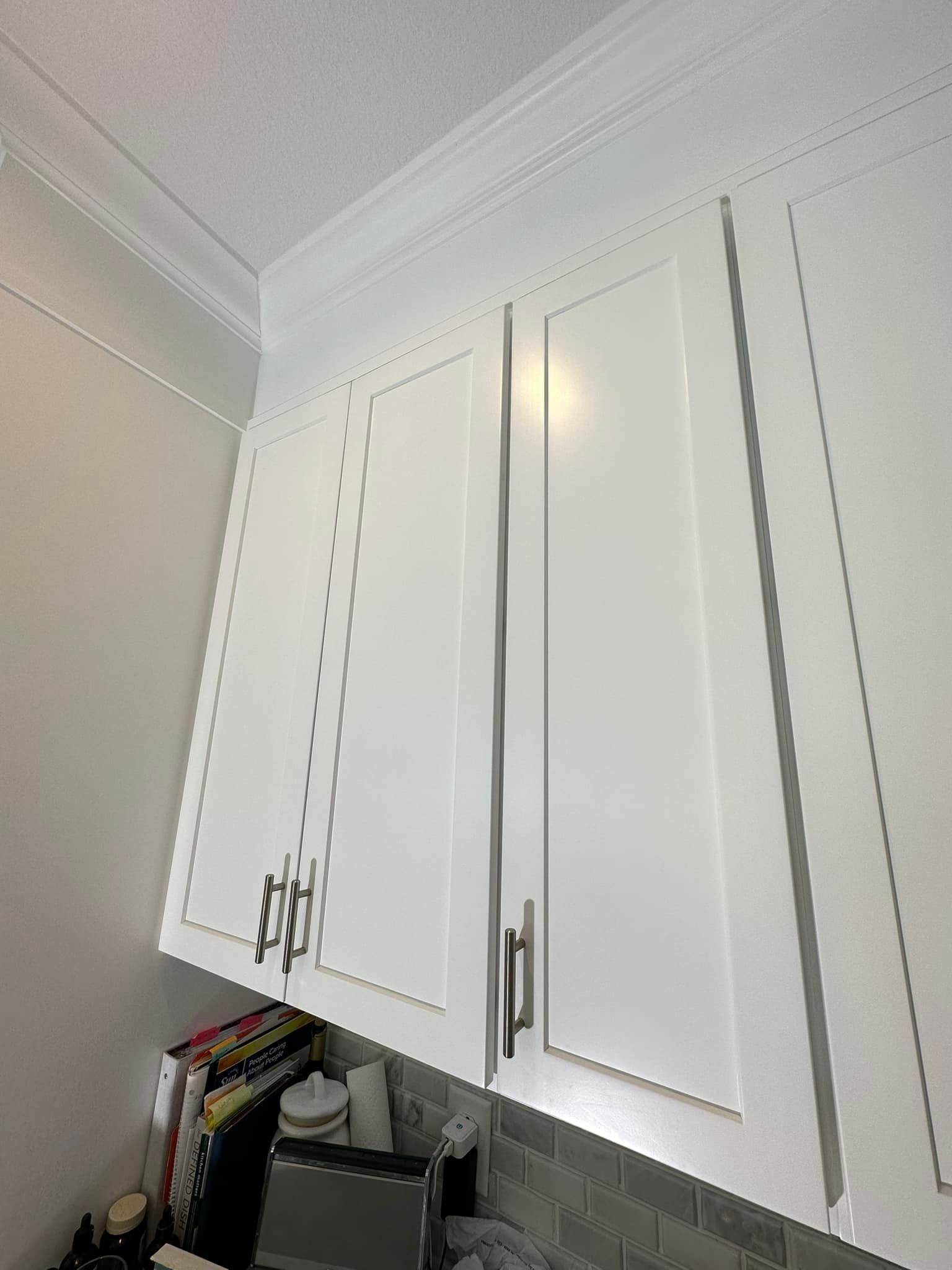 White kitchen cabinets with silver hardware and a white ceiling with crown molding.