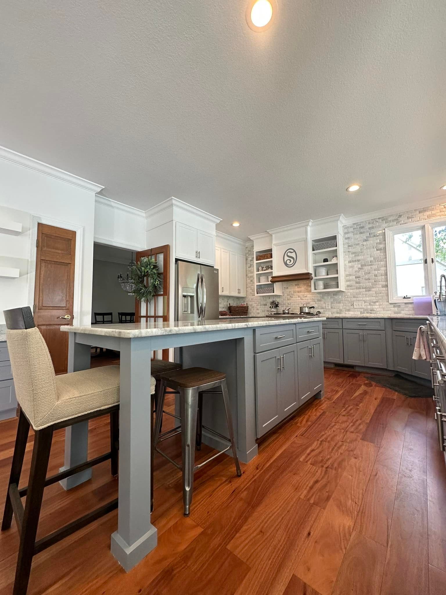 Kitchen with a gray island, wooden floor, and a breakfast bar with two stools.