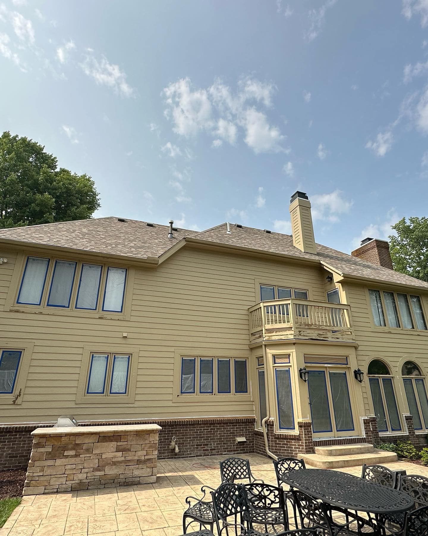 Beige house with patio, outdoor kitchen, and dining set under a partly cloudy sky.