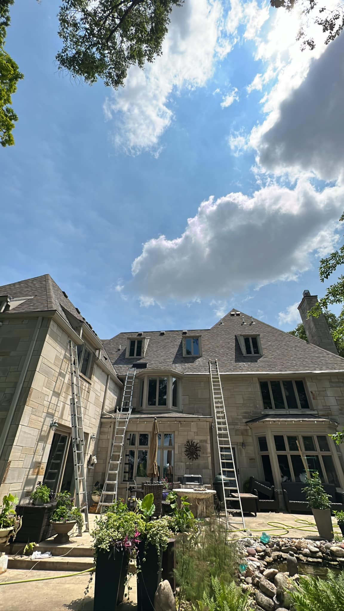 Stone house with ladders against the roof under a blue sky with fluffy clouds.