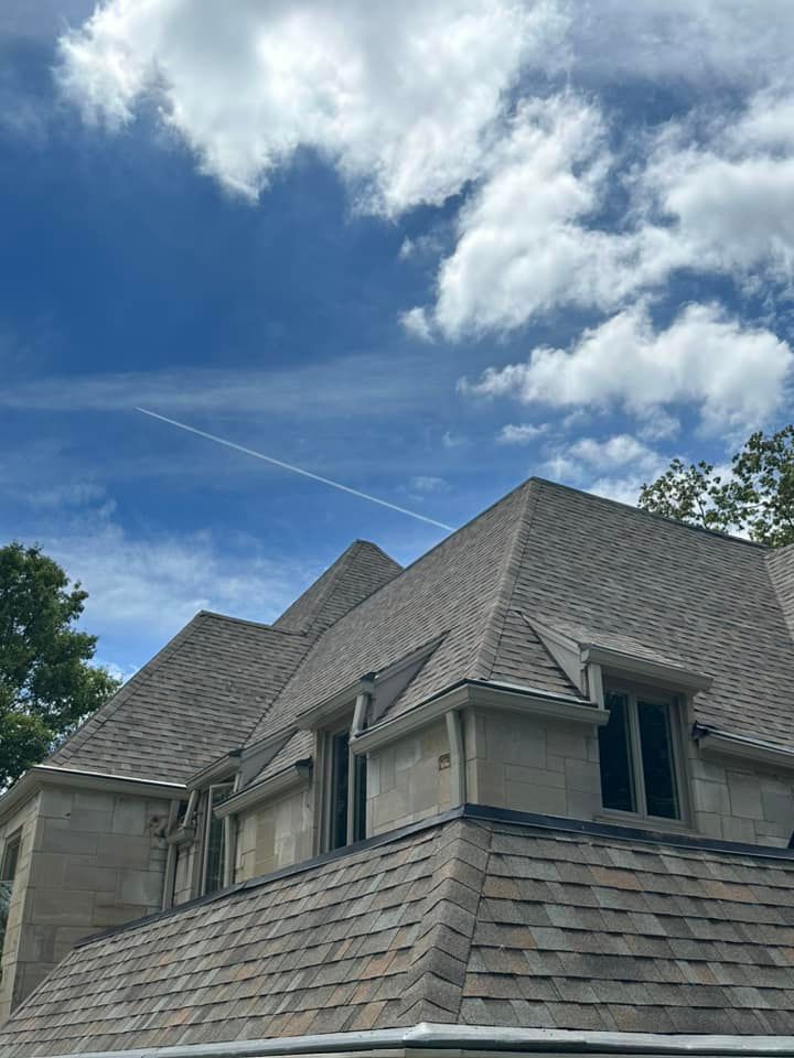 House roof against a blue sky with white clouds; a contrail is visible.