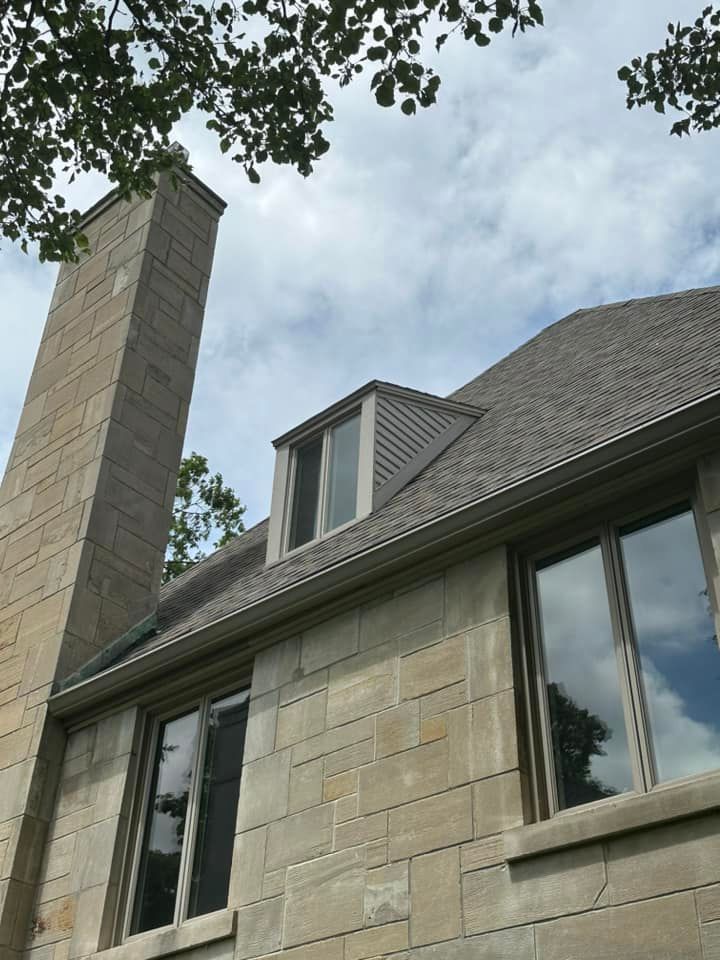 Stone building exterior with chimney, dormer window, and roof under a cloudy sky.