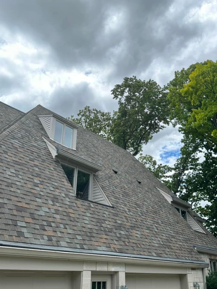 A house with a shingled roof, dormer windows, and a cloudy sky.