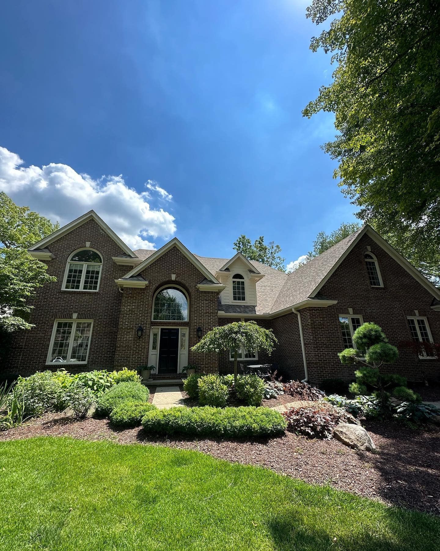 Large brick home with manicured landscaping under a bright blue sky.