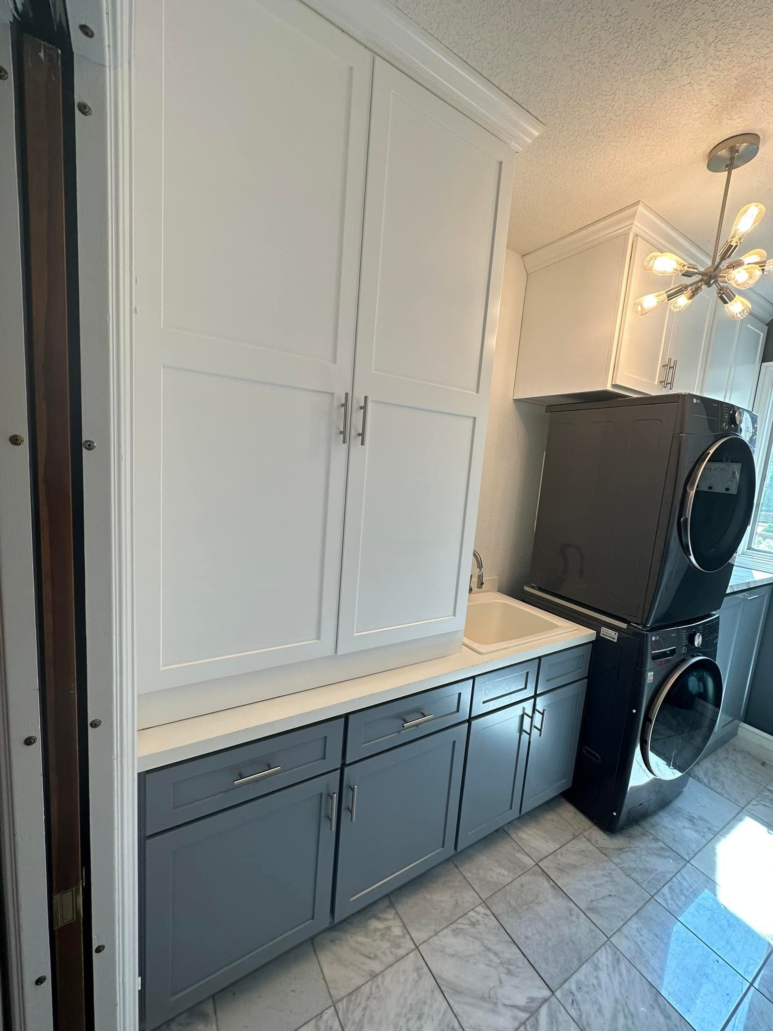 Laundry room with stacked washer/dryer, white and gray cabinets, and a sink.