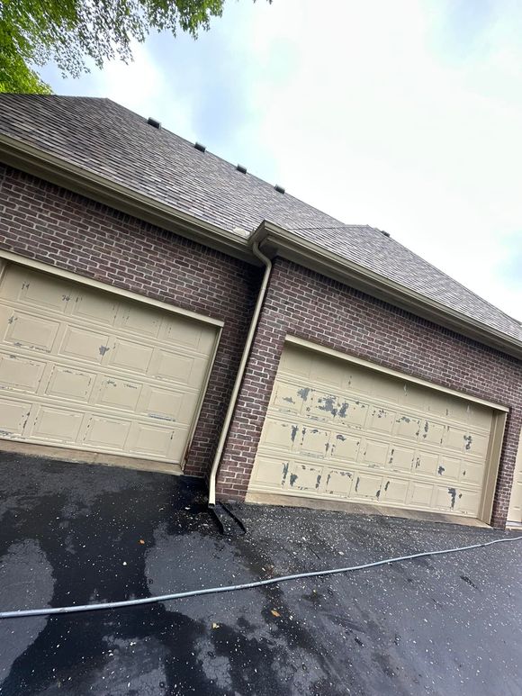 Garage with brown brick exterior, tan garage doors, and a dark asphalt driveway.