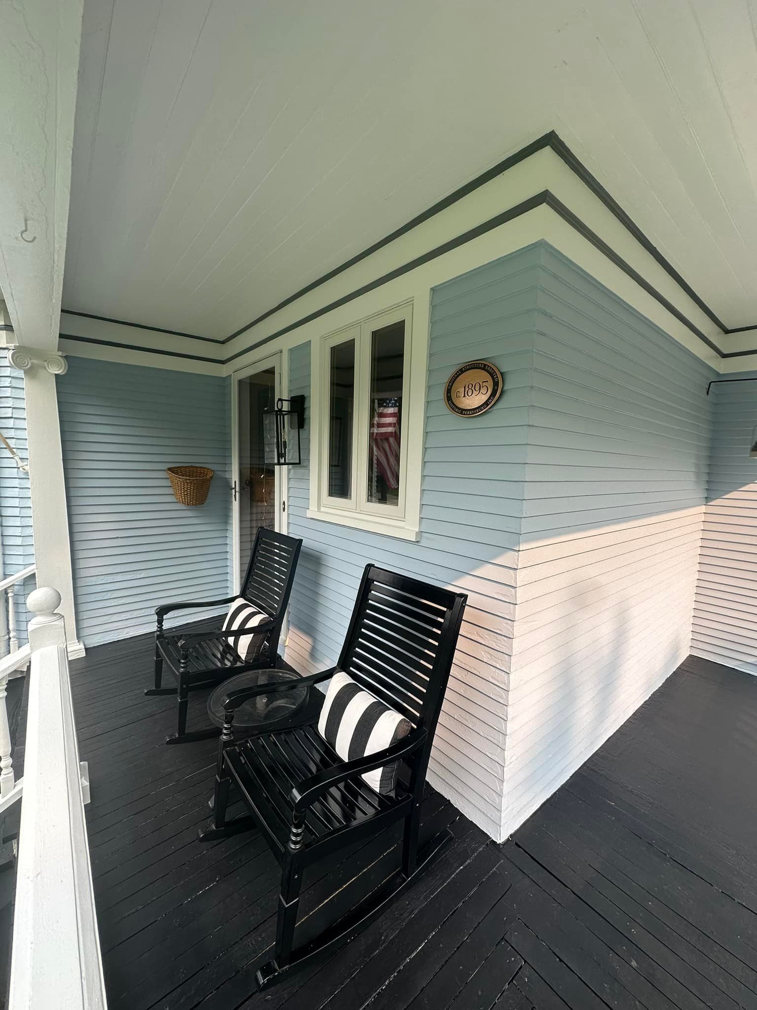 Blue porch with black rocking chairs, black and white striped pillows.