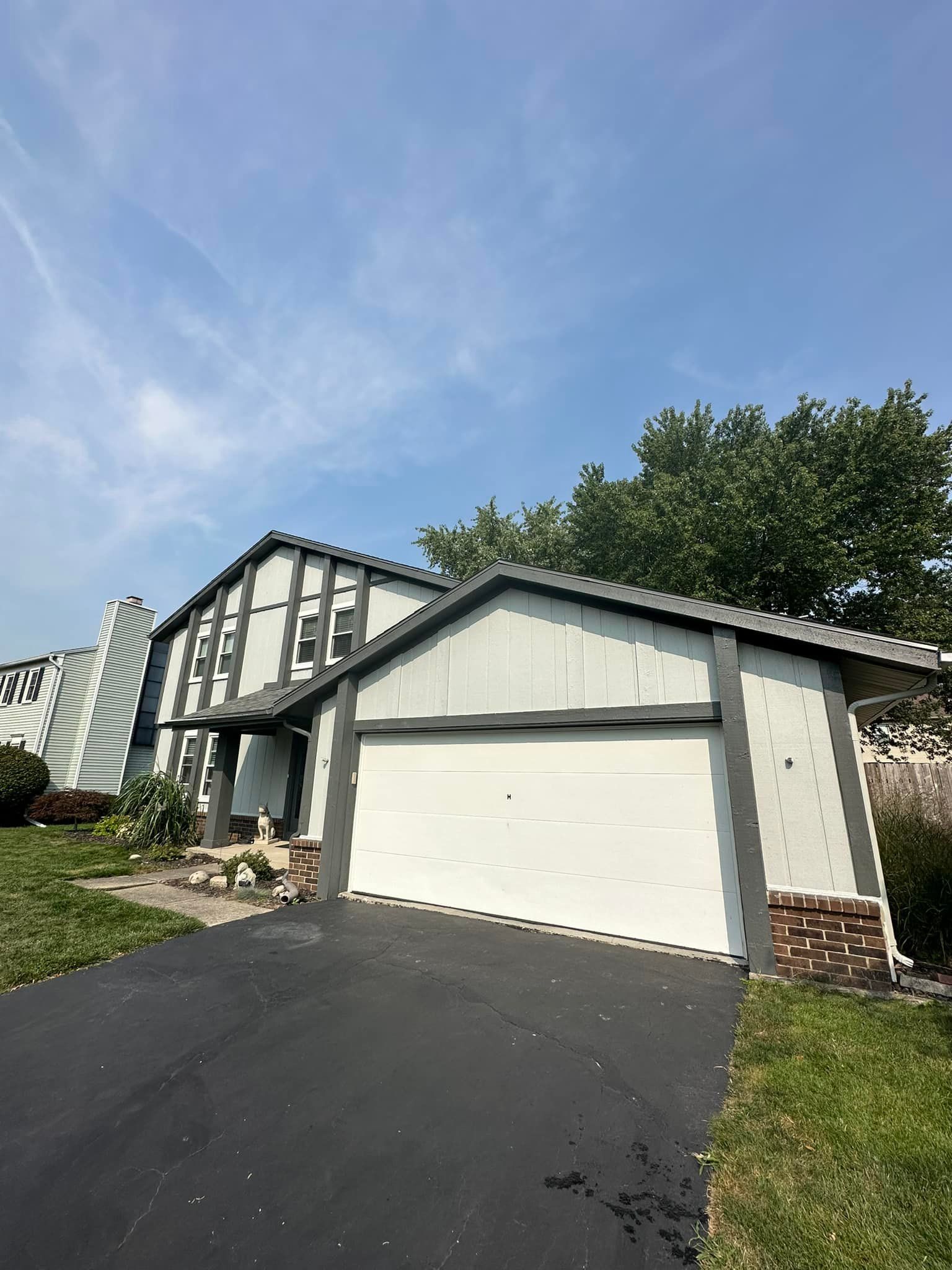 Two-story house with a white garage door, black asphalt driveway, and blue sky.