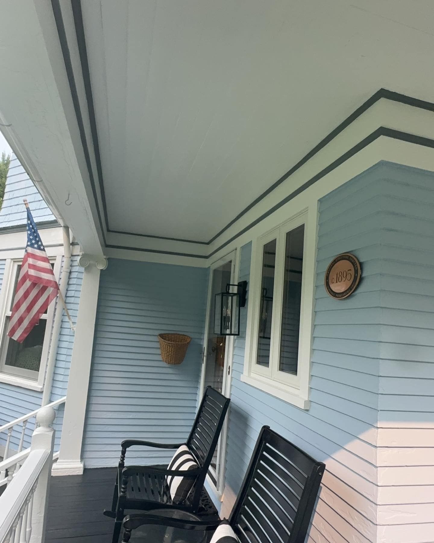 Porch with rocking chairs, light blue siding, American flag, and a wicker basket.