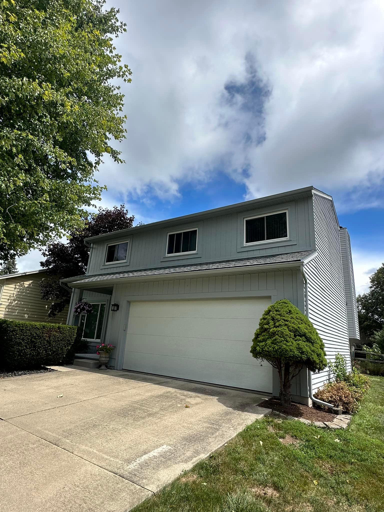 Two-story gray house with a garage, trees, and cloudy sky.