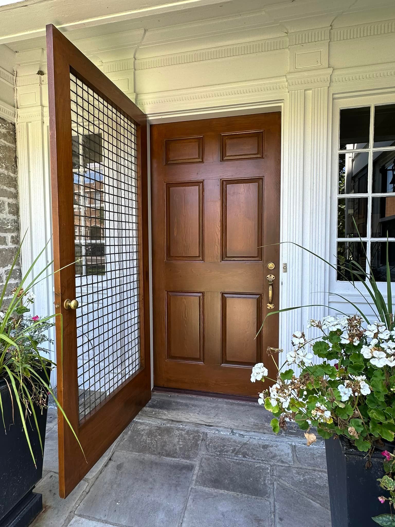 A wooden front door with a decorative glass side panel is partially open, revealing a stone entryway and plants.