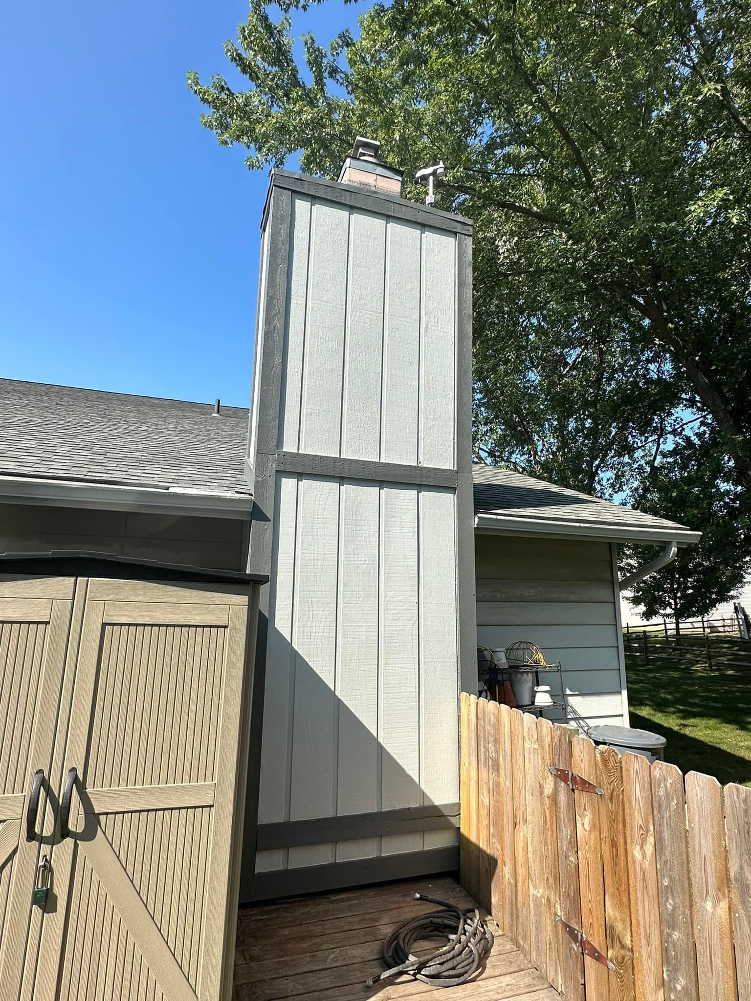 Chimney against a blue sky, beside a shed and wooden fence.