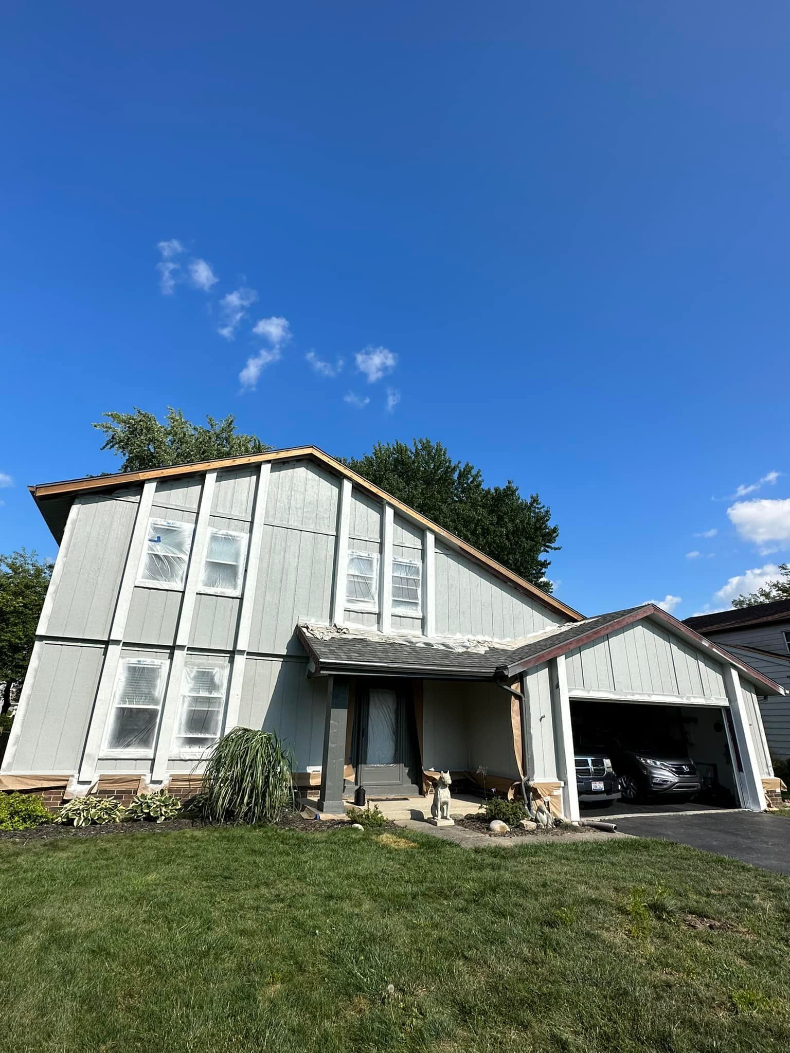 Two-story gray house with carport, green grass, and blue sky.