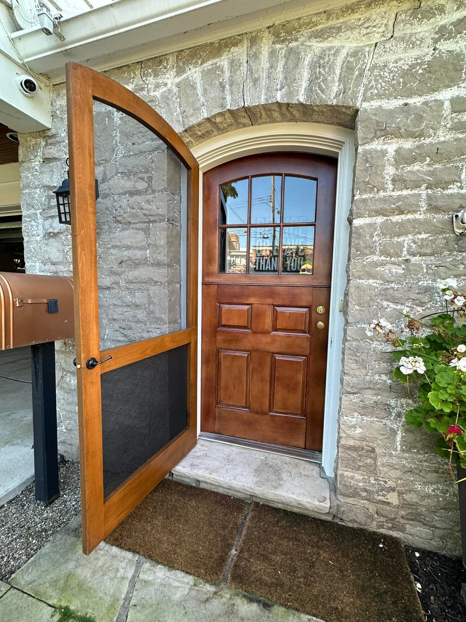 Wooden door with screen door open in a stone building. Doorway has a small stoop and a welcome mat.