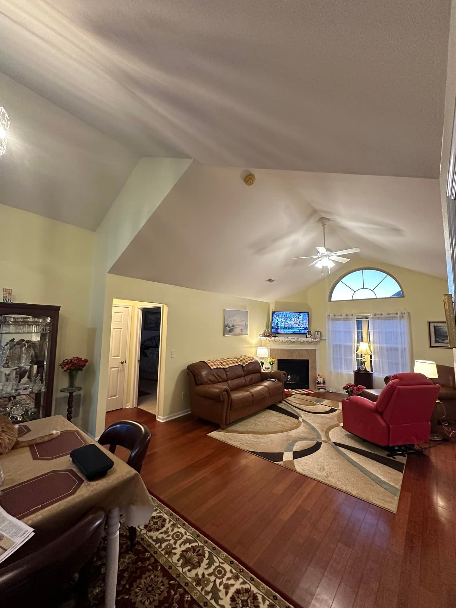 Living room with leather sofa, red recliner, fireplace, arched window, and hardwood floors.