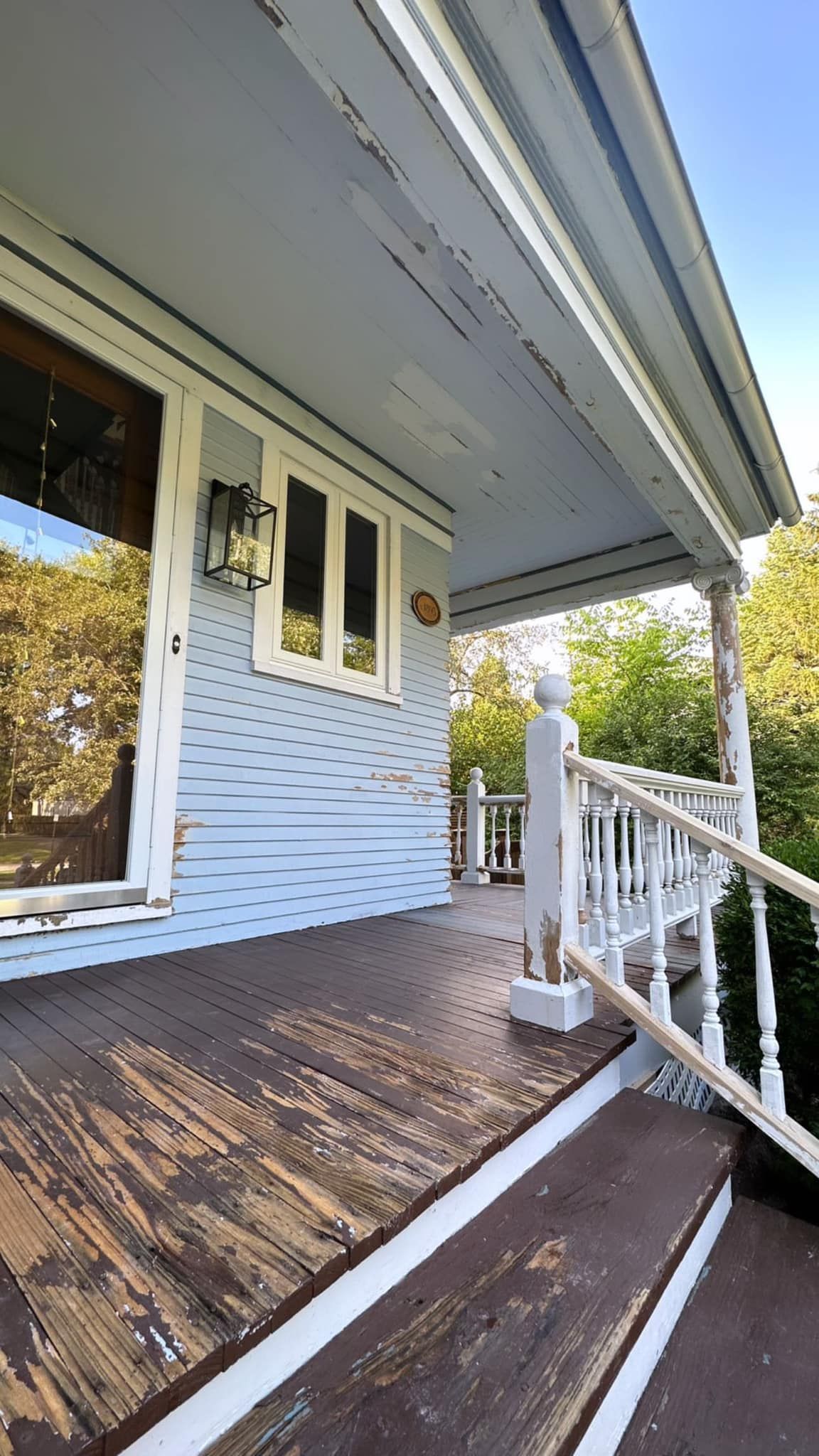 Blue and white porch with peeling paint. Includes windows, railing, and a light fixture.