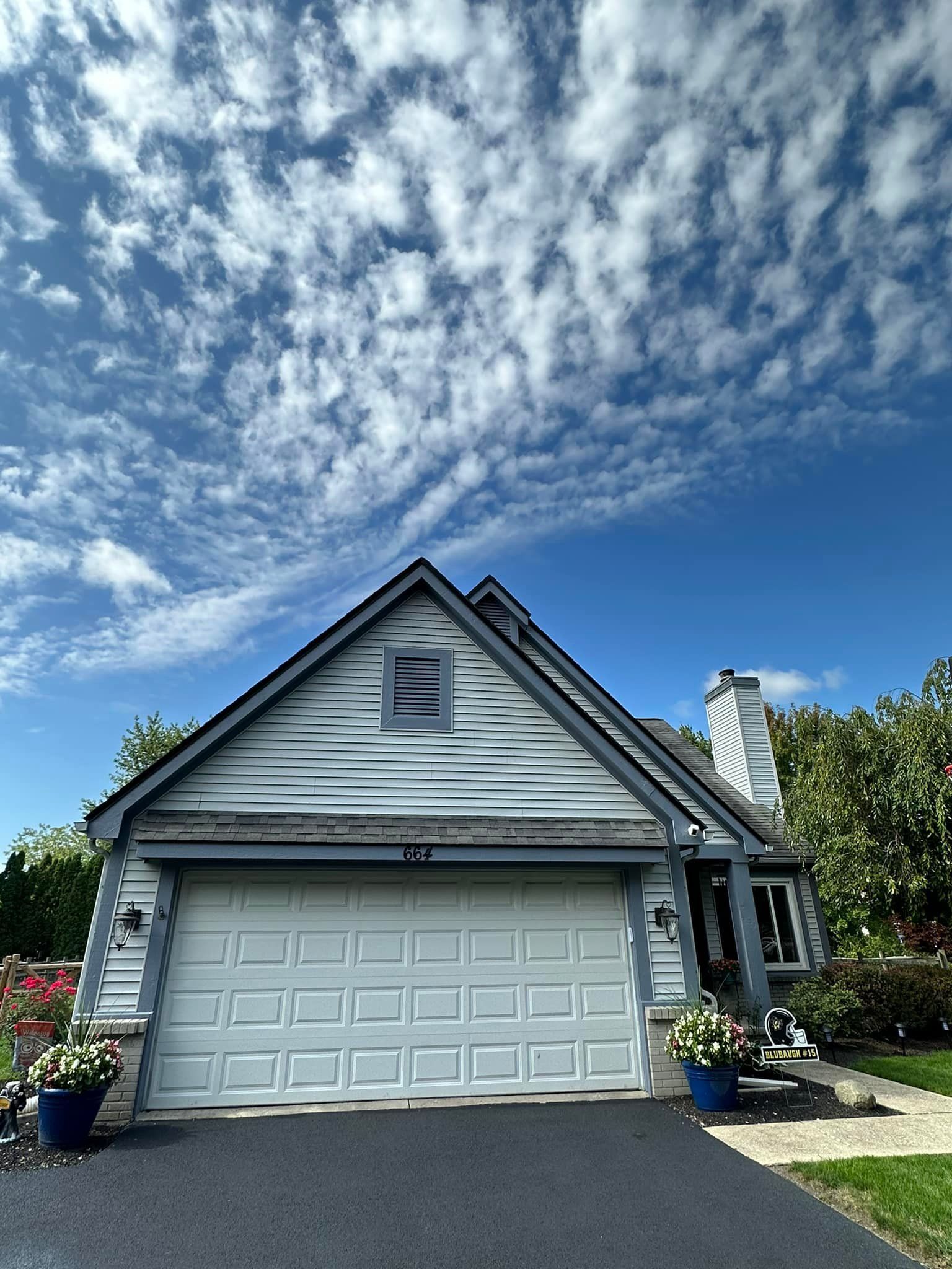 Blue-sided house with white garage door, under a blue sky dotted with white clouds.