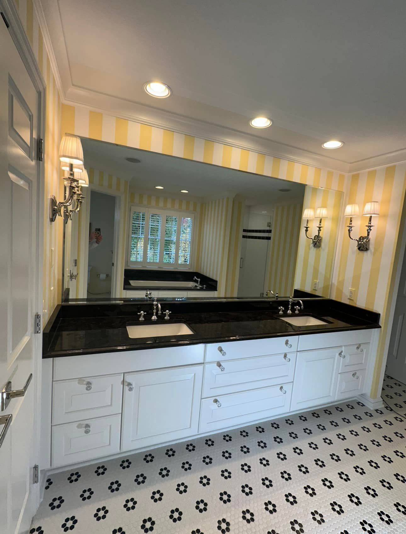 Bathroom with white cabinets, black countertop, yellow striped walls, large mirror, and patterned tile floor.