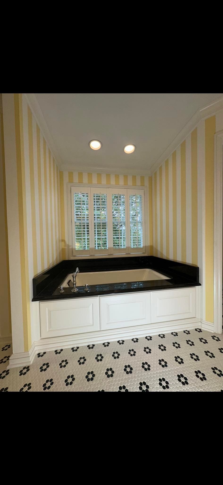 Bathroom with yellow striped walls, a white-tiled tub with black countertop, and a window.