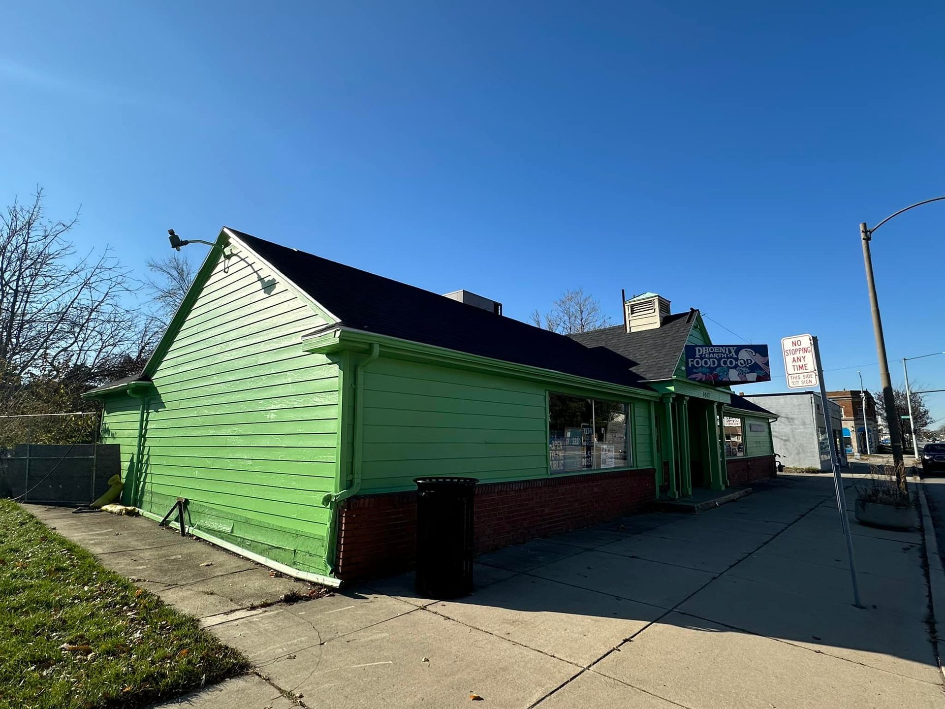 Green building with a black roof, sign, and brick facade on a sunny day.