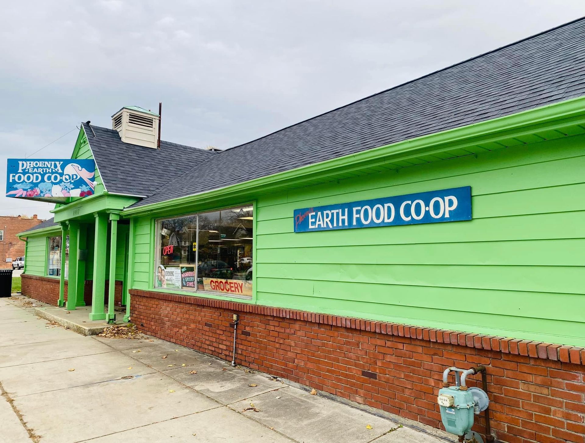 Green Earth Food Co-op building with blue signage, red brick, and dark roof. Cloudy day.