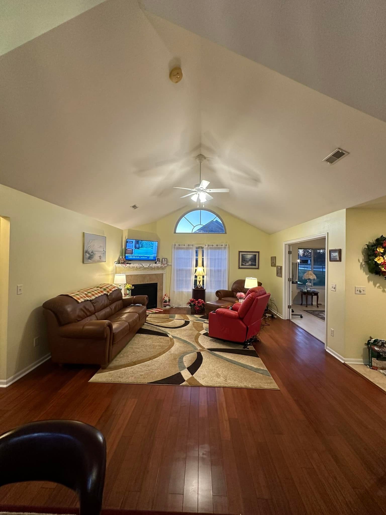 Living room with high ceiling, brown leather sofa, red recliner, fireplace, hardwood floors, and a patterned rug.
