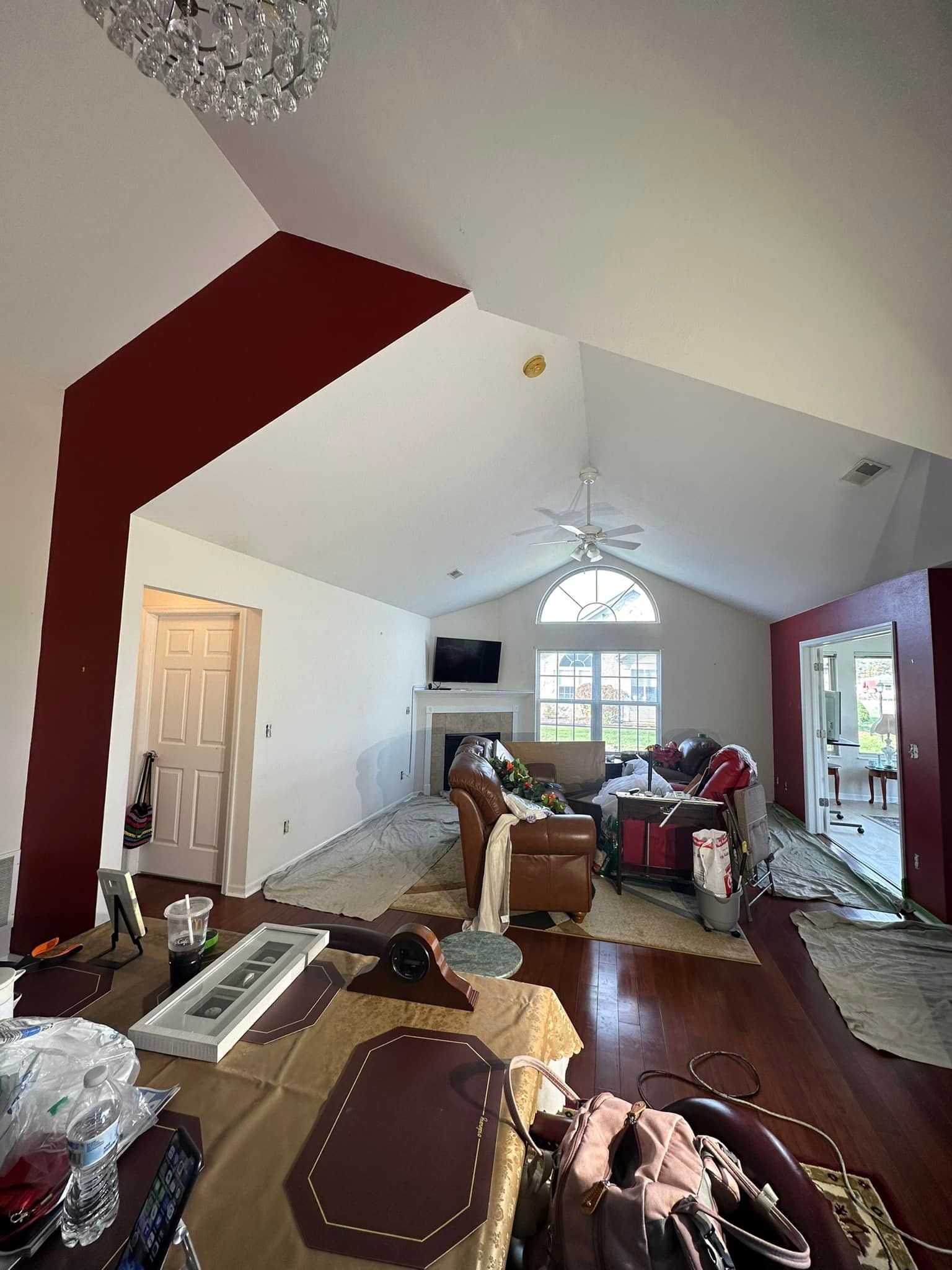 Interior of a living room with vaulted ceilings and a red accent wall, cluttered with furniture and supplies.
