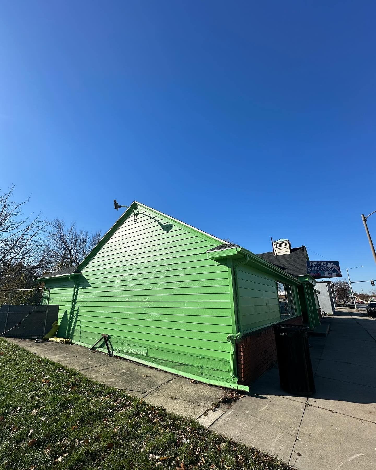 Green building with a slanted roof, next to a sidewalk on a sunny day.
