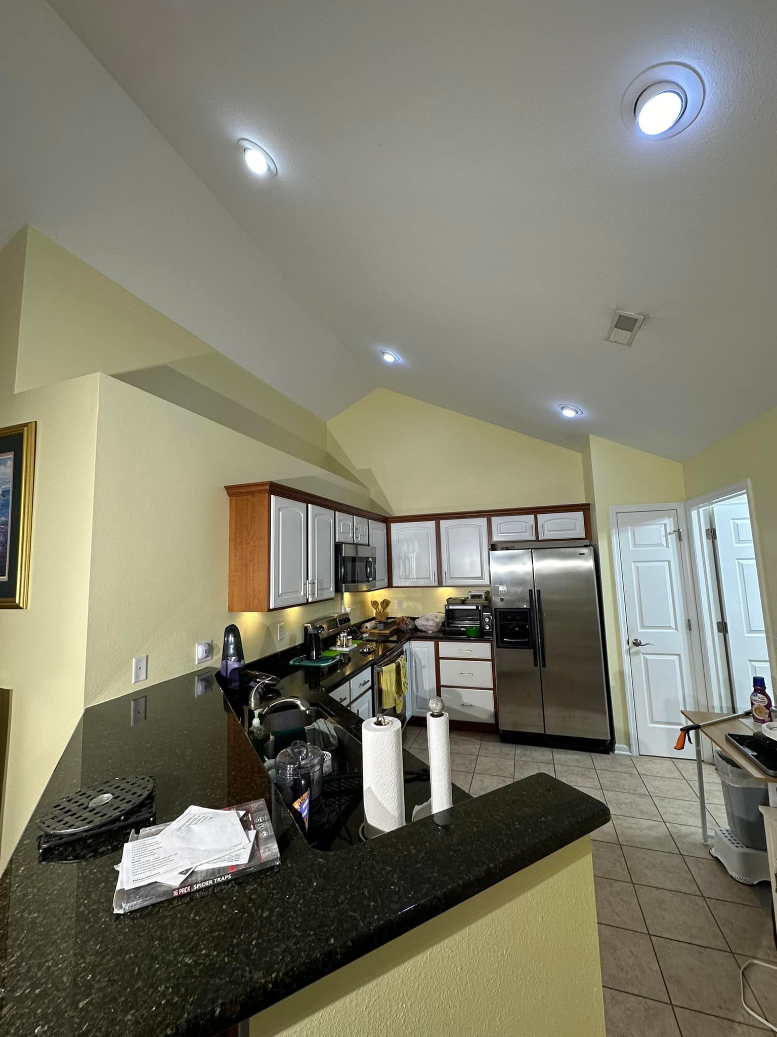 Kitchen with black countertop, white and wood cabinets, and stainless steel refrigerator.