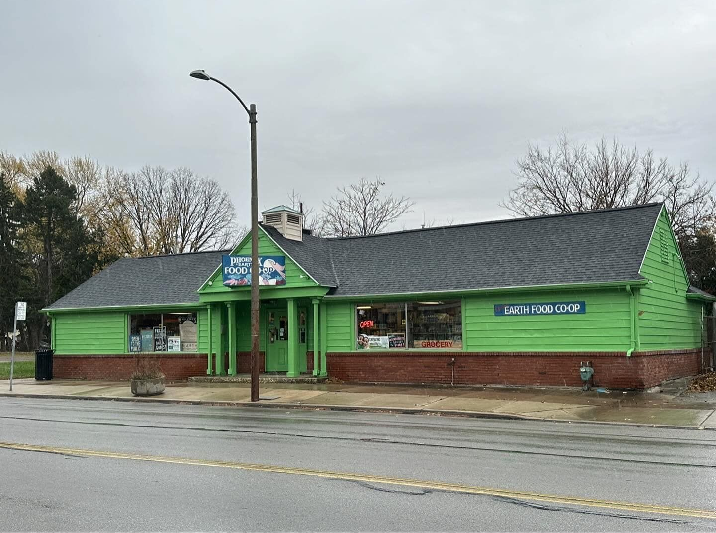 Green-painted single-story building; brick base; sign above door. Cloudy sky, wet road.
