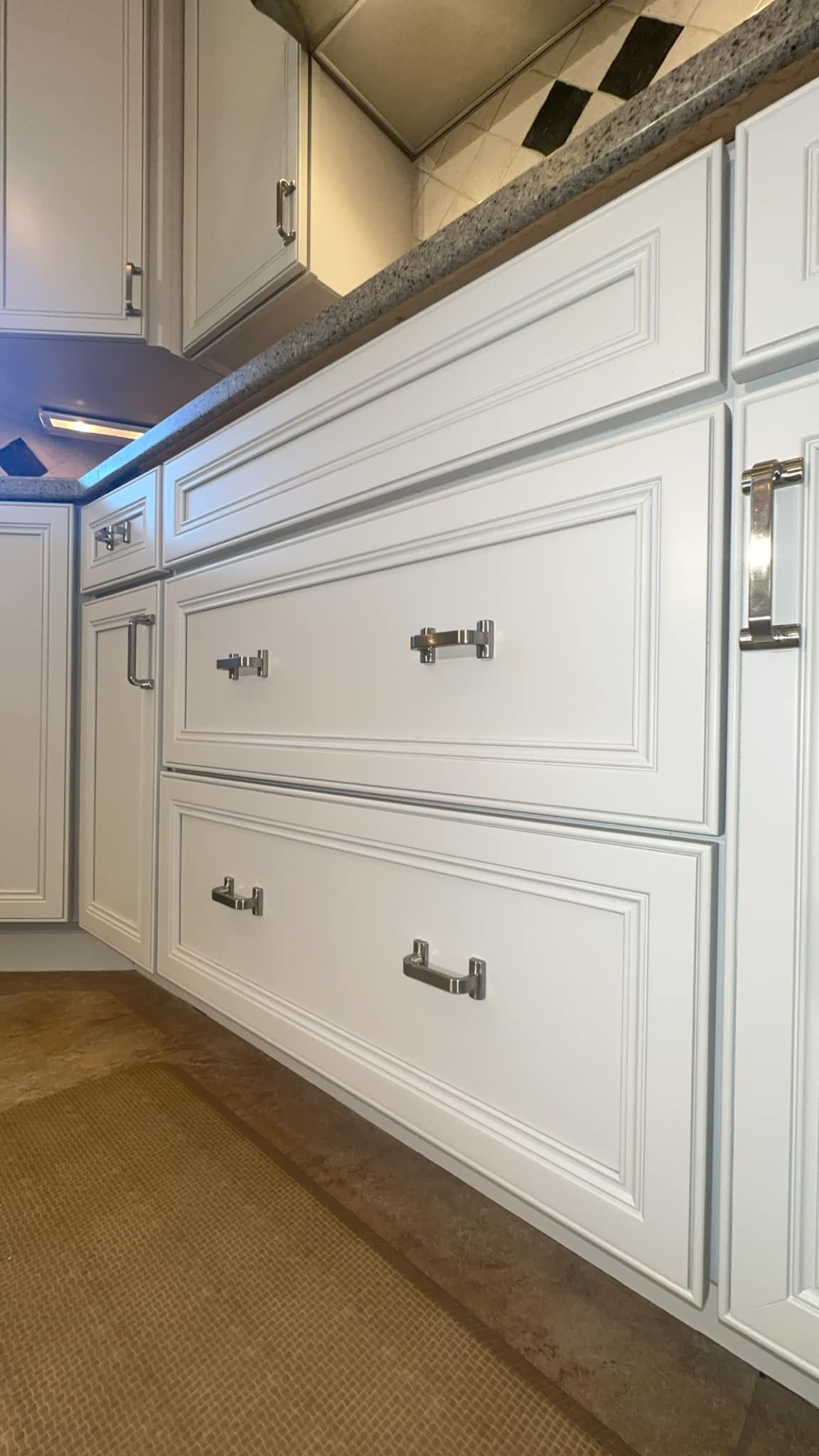 White kitchen cabinets with silver hardware and a granite countertop.
