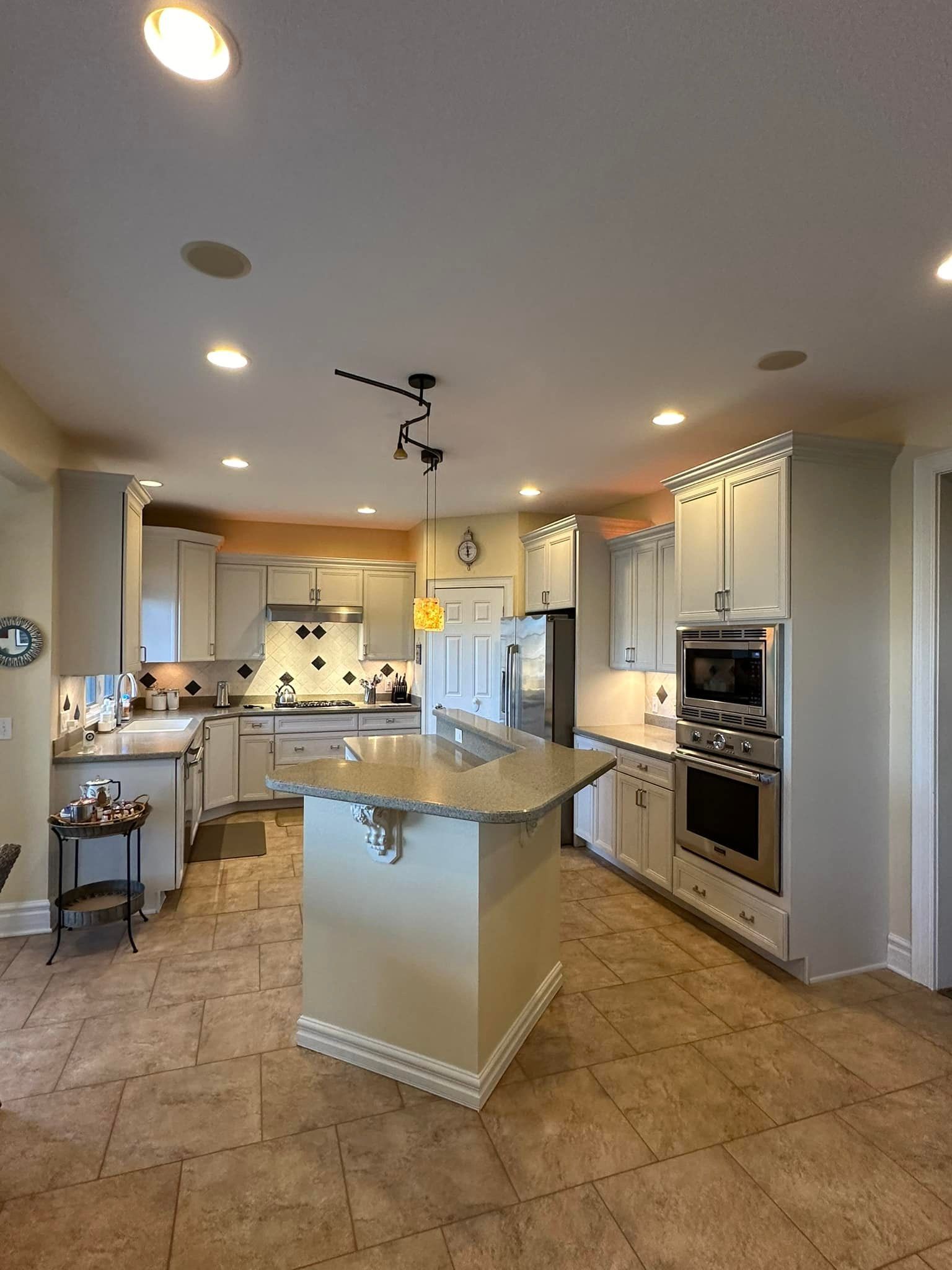 Spacious kitchen with a central island, light cabinets, stainless steel appliances, and tile flooring.