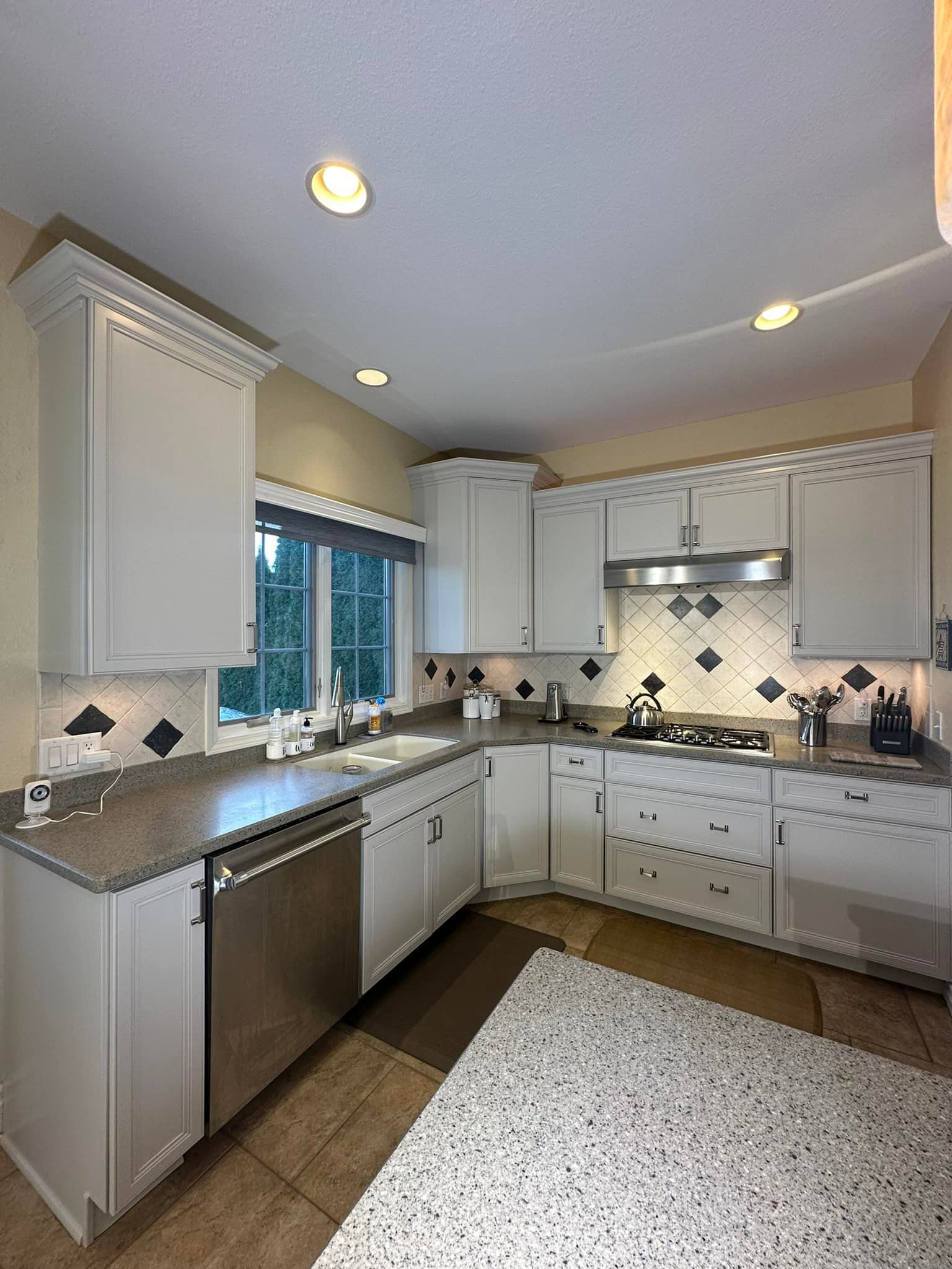 White kitchen with stainless steel appliances, white cabinets, and patterned backsplash.