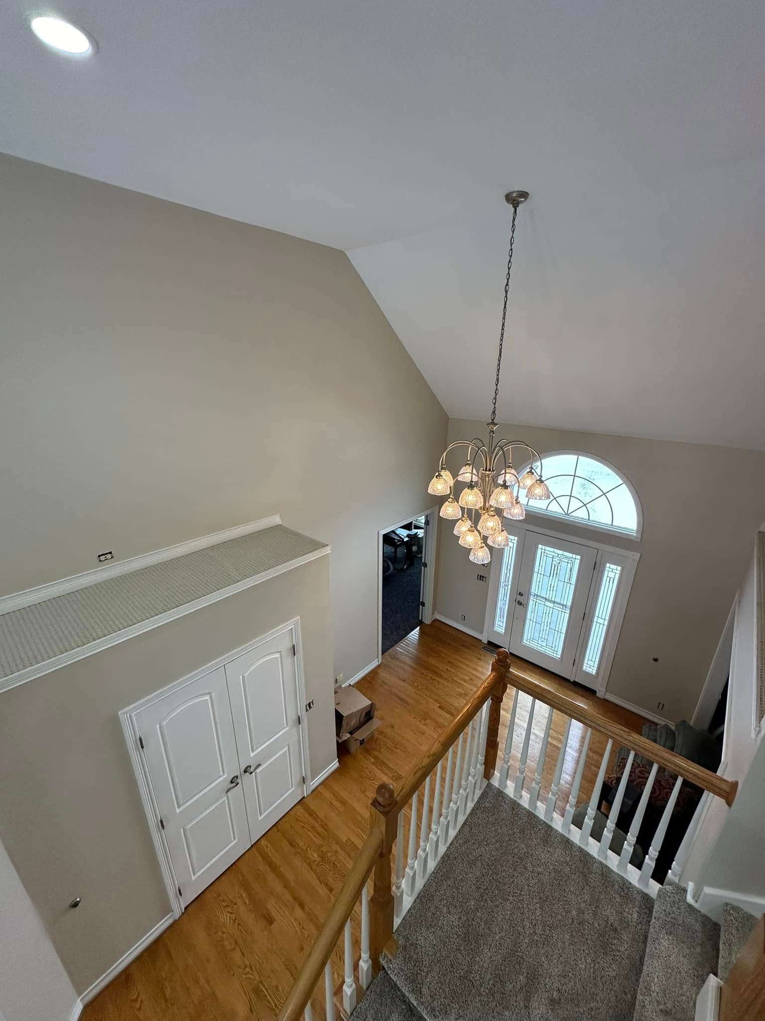 High-angle view of a home entryway with a chandelier, two doors, and a staircase with wood and white accents.