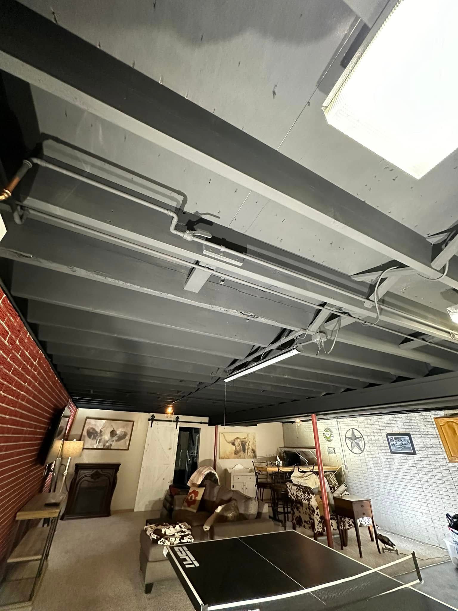 Basement ceiling with painted beams, ping pong table, brick wall, and various furnishings.