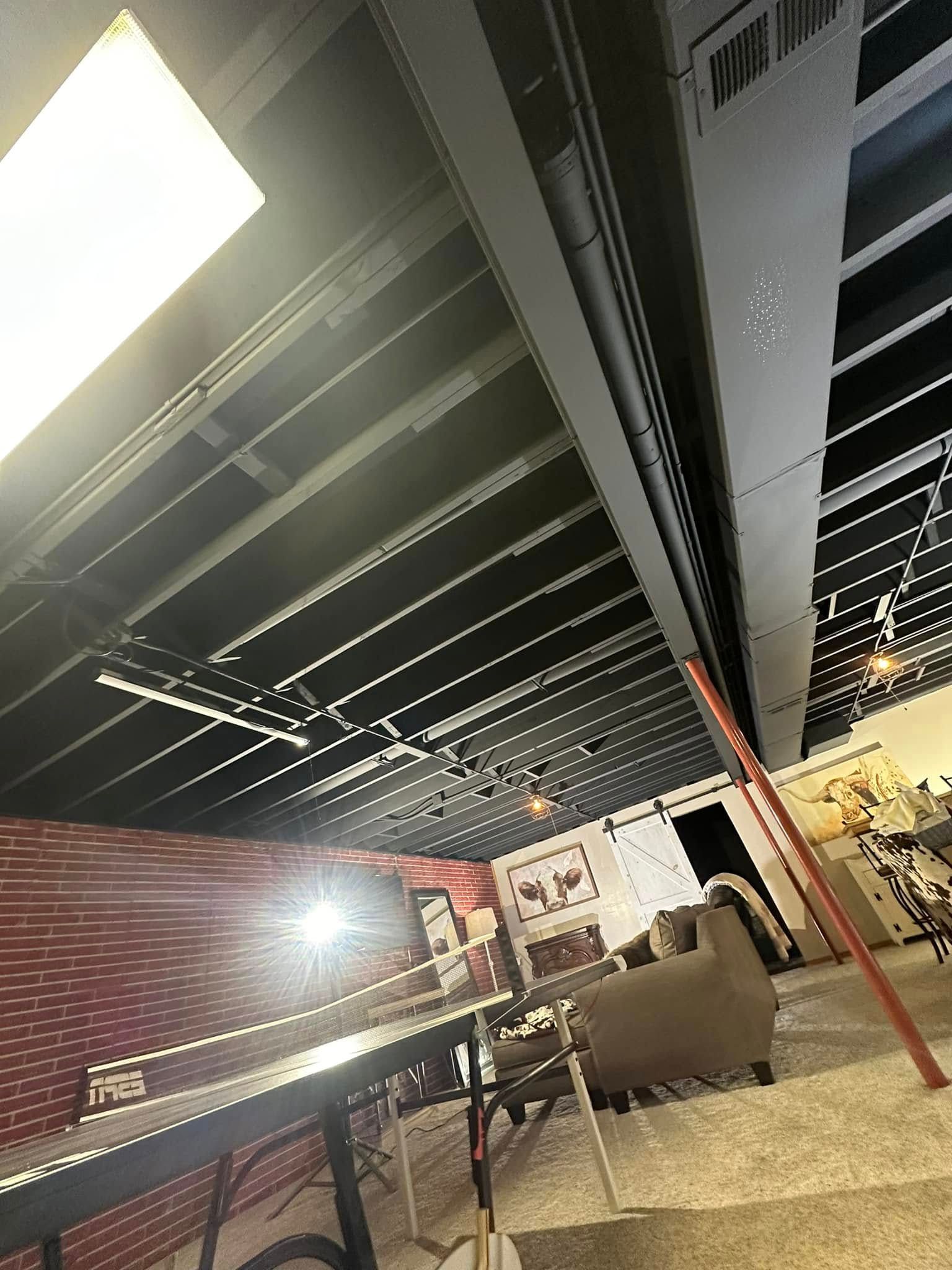 Black ceiling with exposed beams, light fixture, room with a table, chair, couch, and wall art.