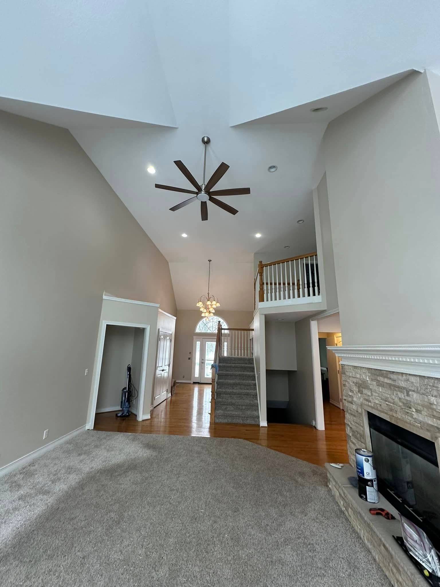 Spacious living room with high ceilings, fan, fireplace, and stairs leading to a second floor.