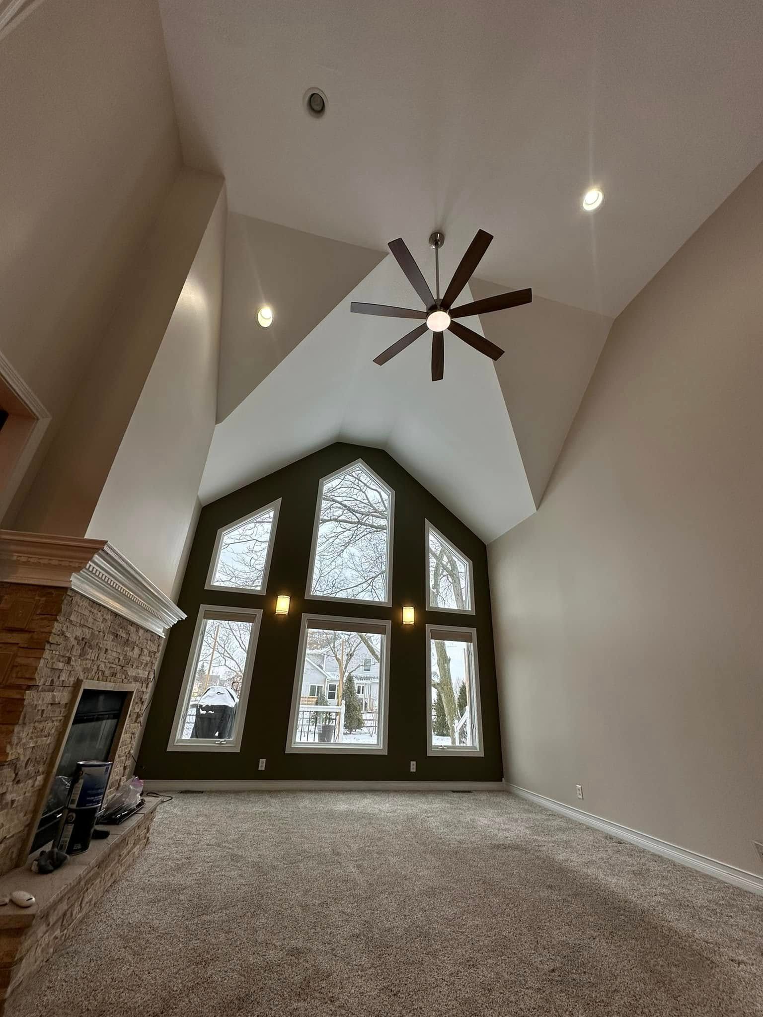 Living room with high ceiling, large windows, fireplace, and a ceiling fan.