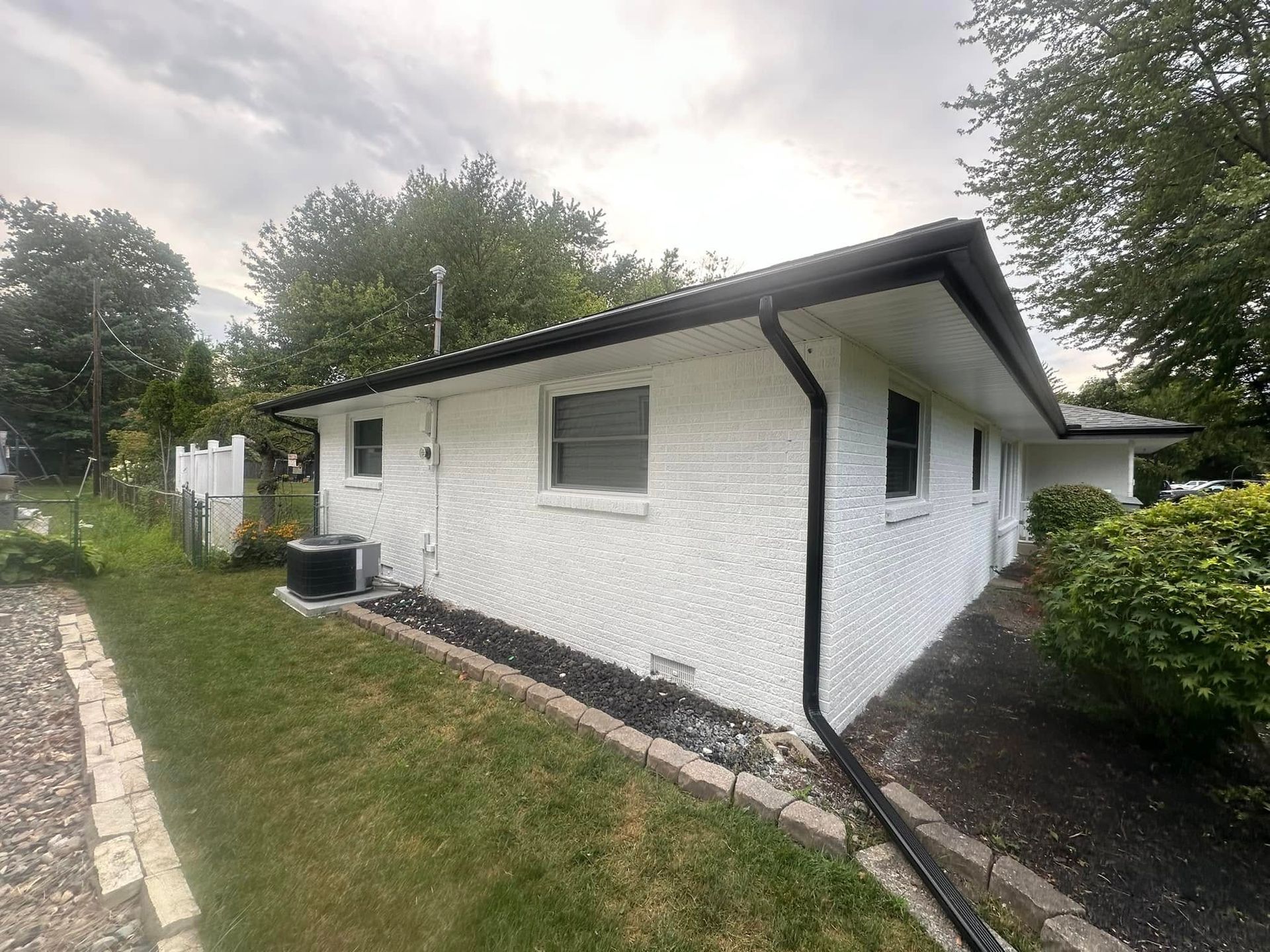 White house with black trim and gutters, small windows, on a grassy lot.